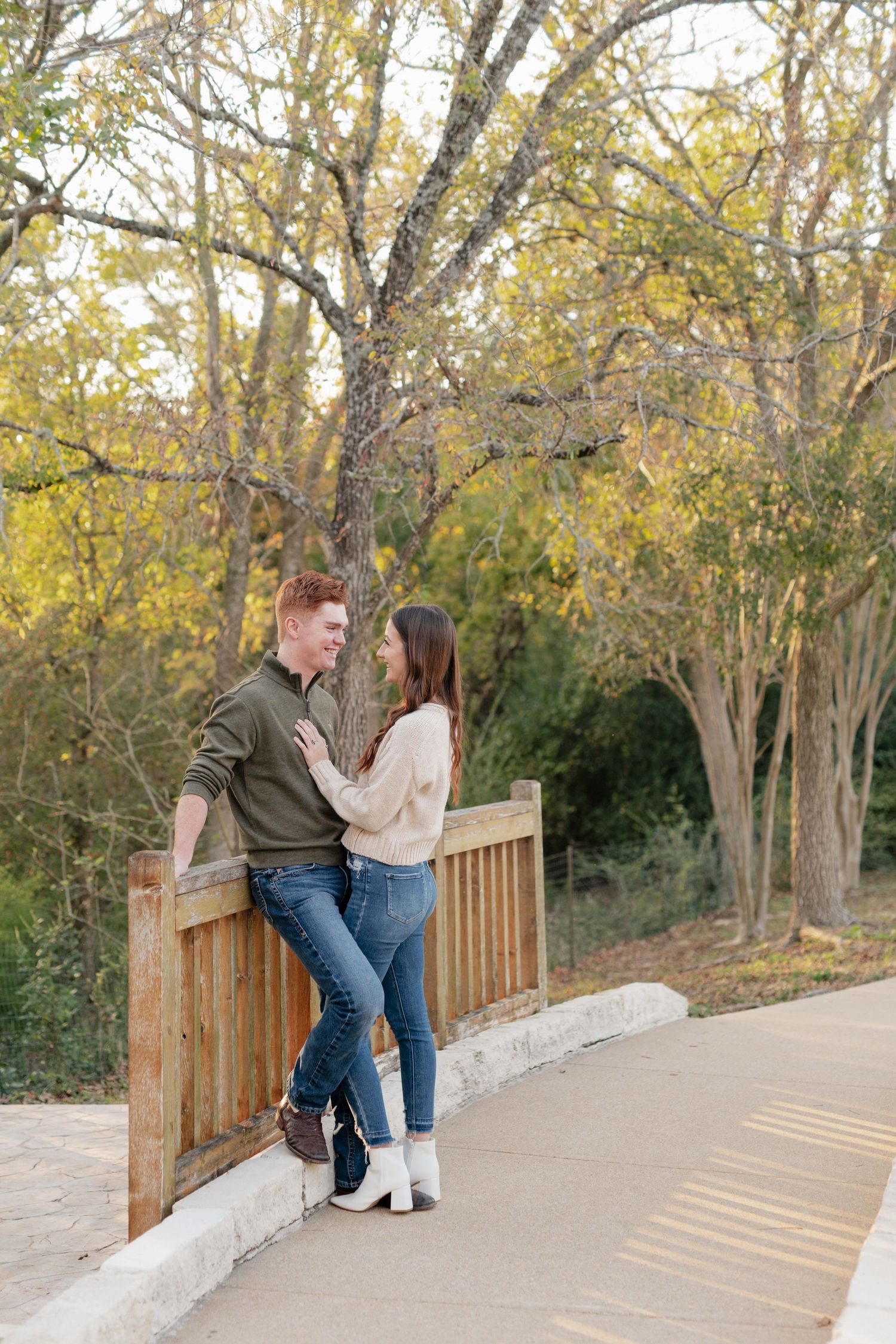 Couple poses together on a wooden bridge surrounded by autumn trees.