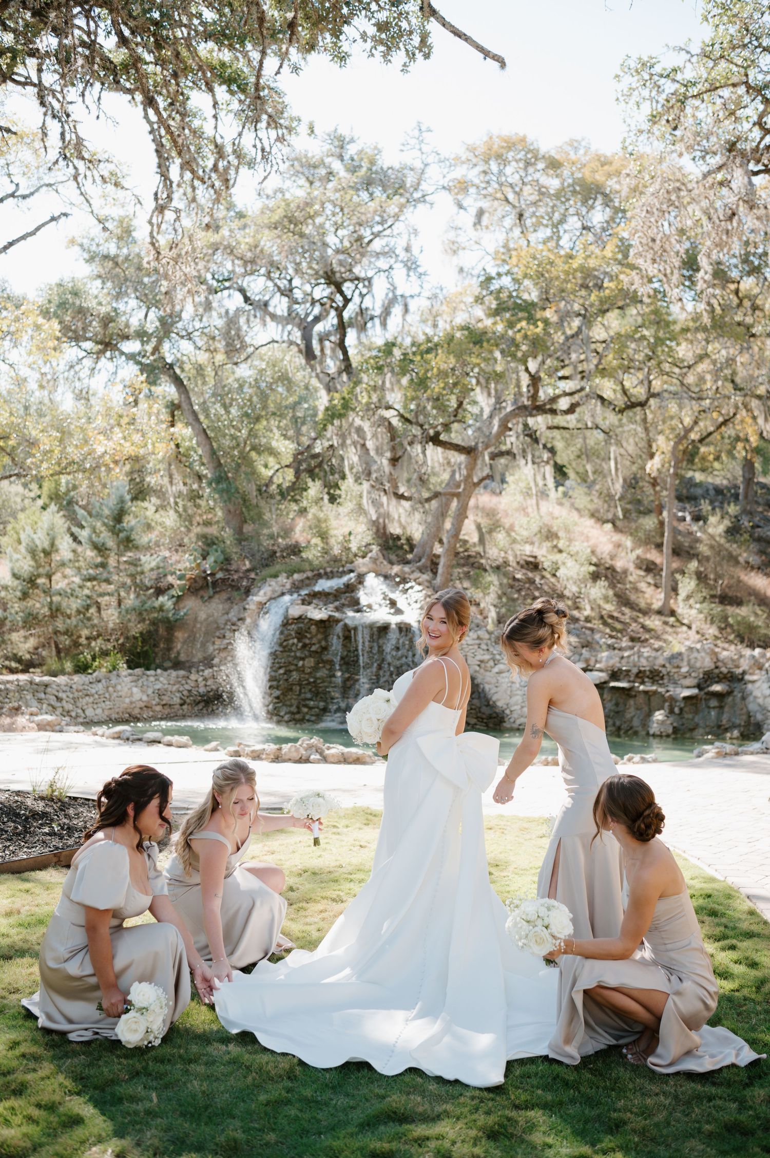 Wedding party relaxing on grass under oak trees during an outdoor photo session.
