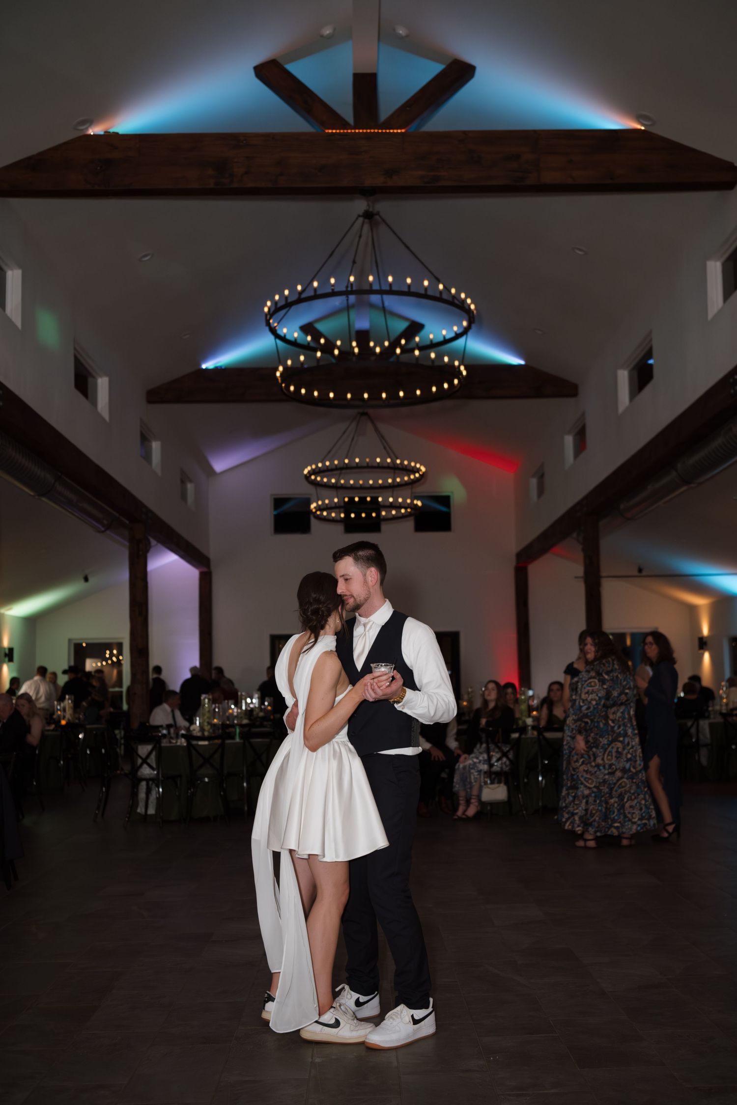 Wedding couple shares a romantic dance under circular chandeliers with colored mood lighting.