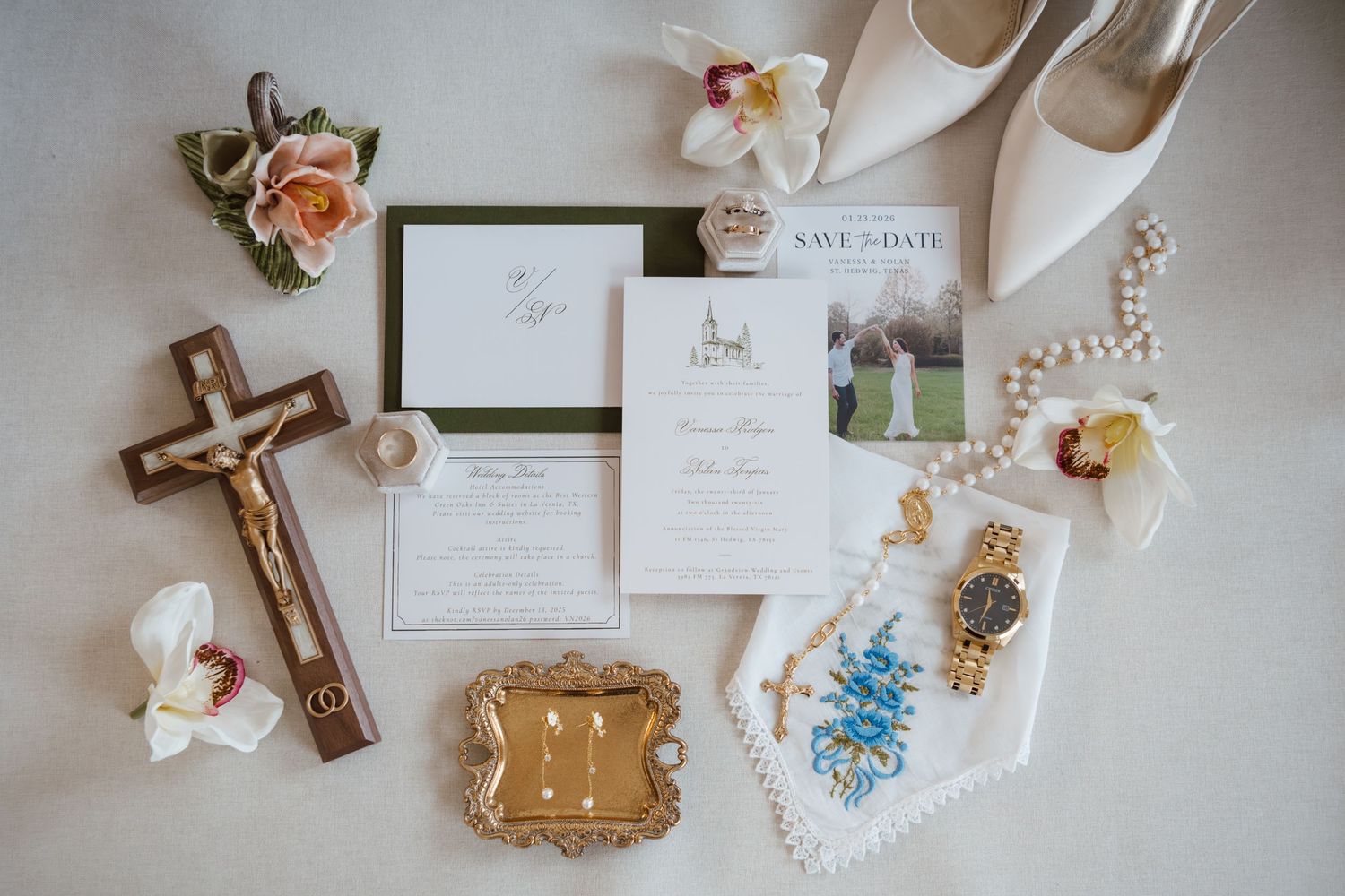 Elegant wedding details flatlay with invitations, rings, flowers, and decorative elements on light neutral background.