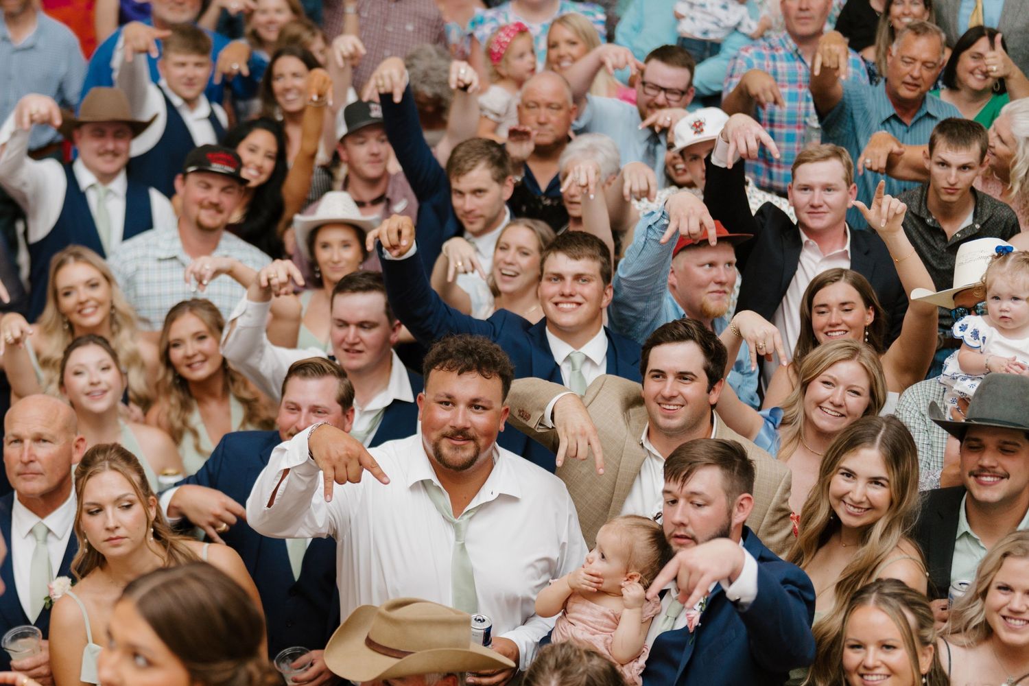 Large crowd of wedding guests cheering and celebrating during reception festivities.