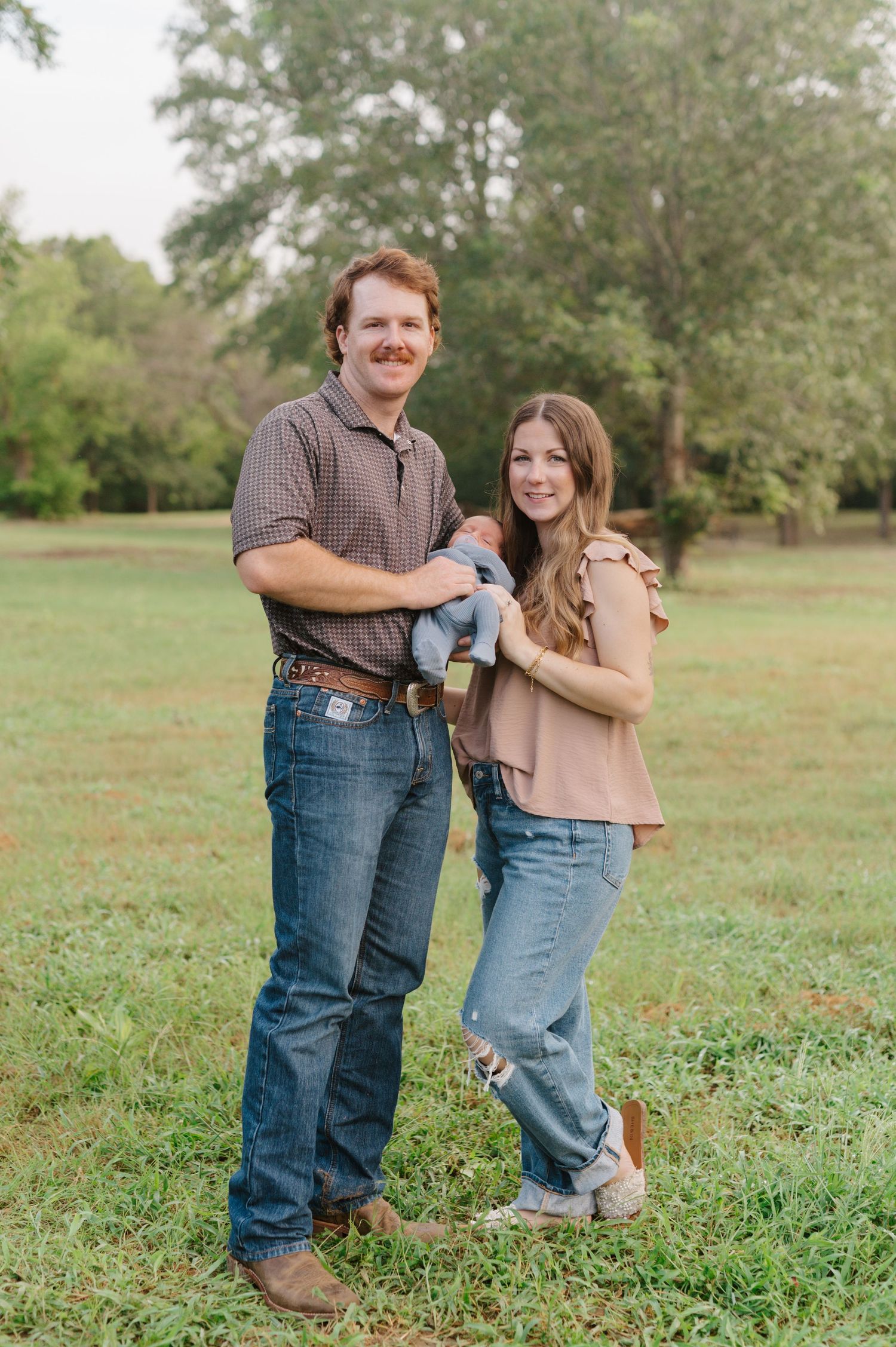 A couple shares playful moments together in a grassy field while wearing casual clothing and denim.
