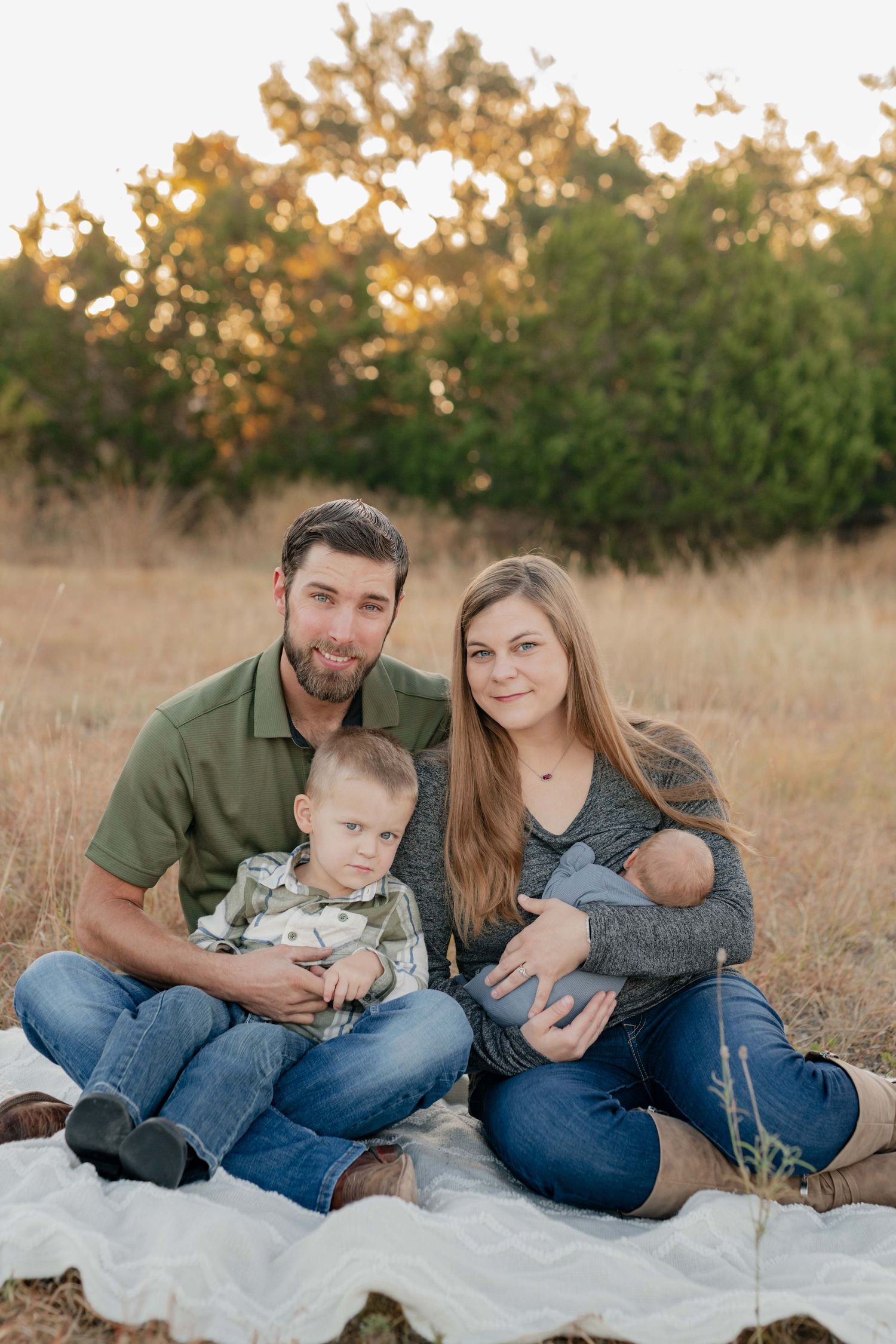 Family sitting together on blanket in autumn field during sunset portrait session.