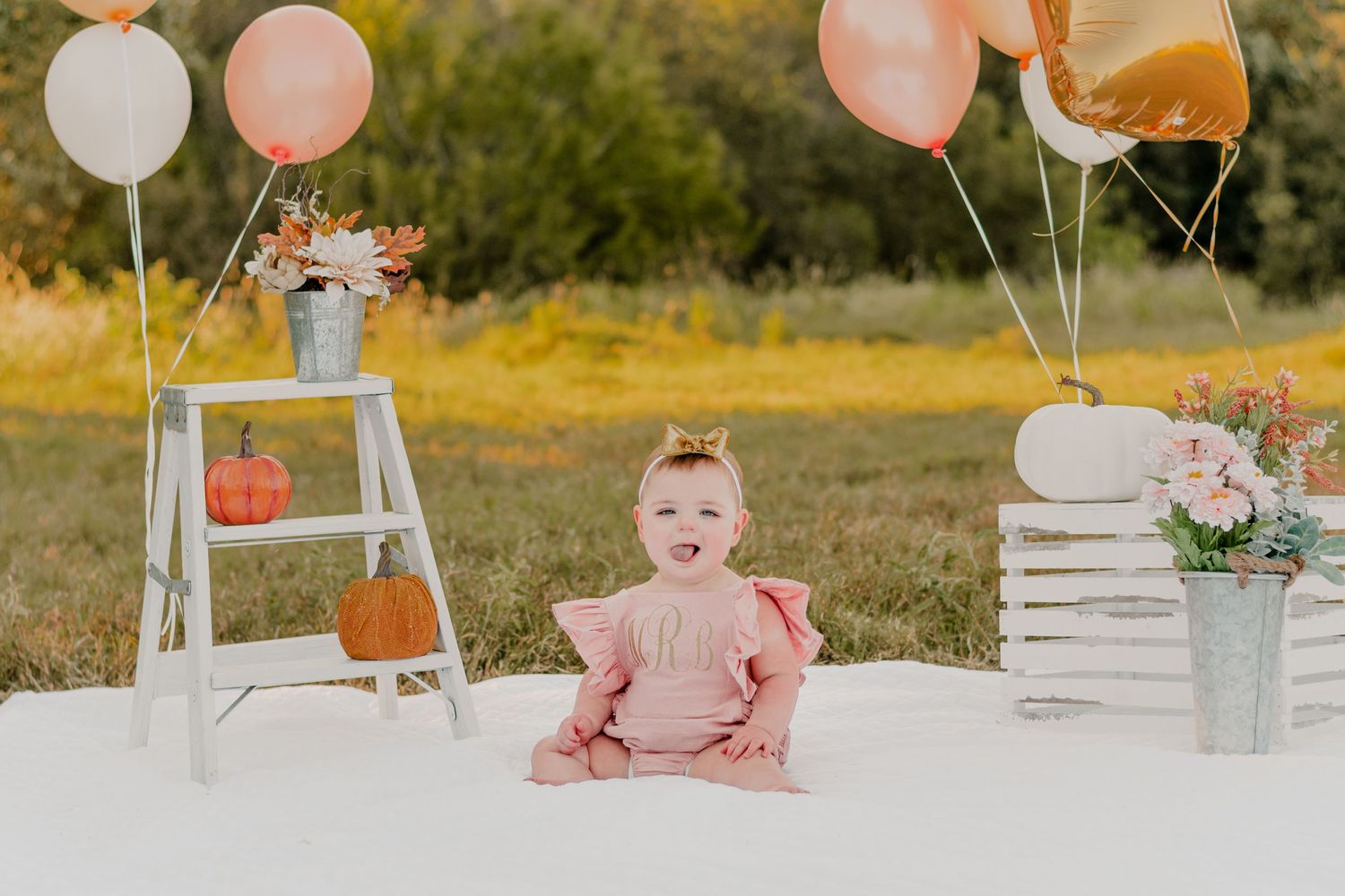 Outdoor birthday setup with white blanket, pastel balloons, vintage ladder decor and floral arrangements in fall setting.