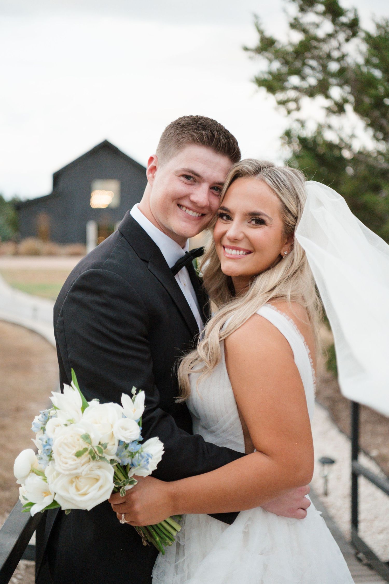 A bride and groom embracing each other in a romantic outdoor wedding setting, with the bride wearing a white wedding dress.