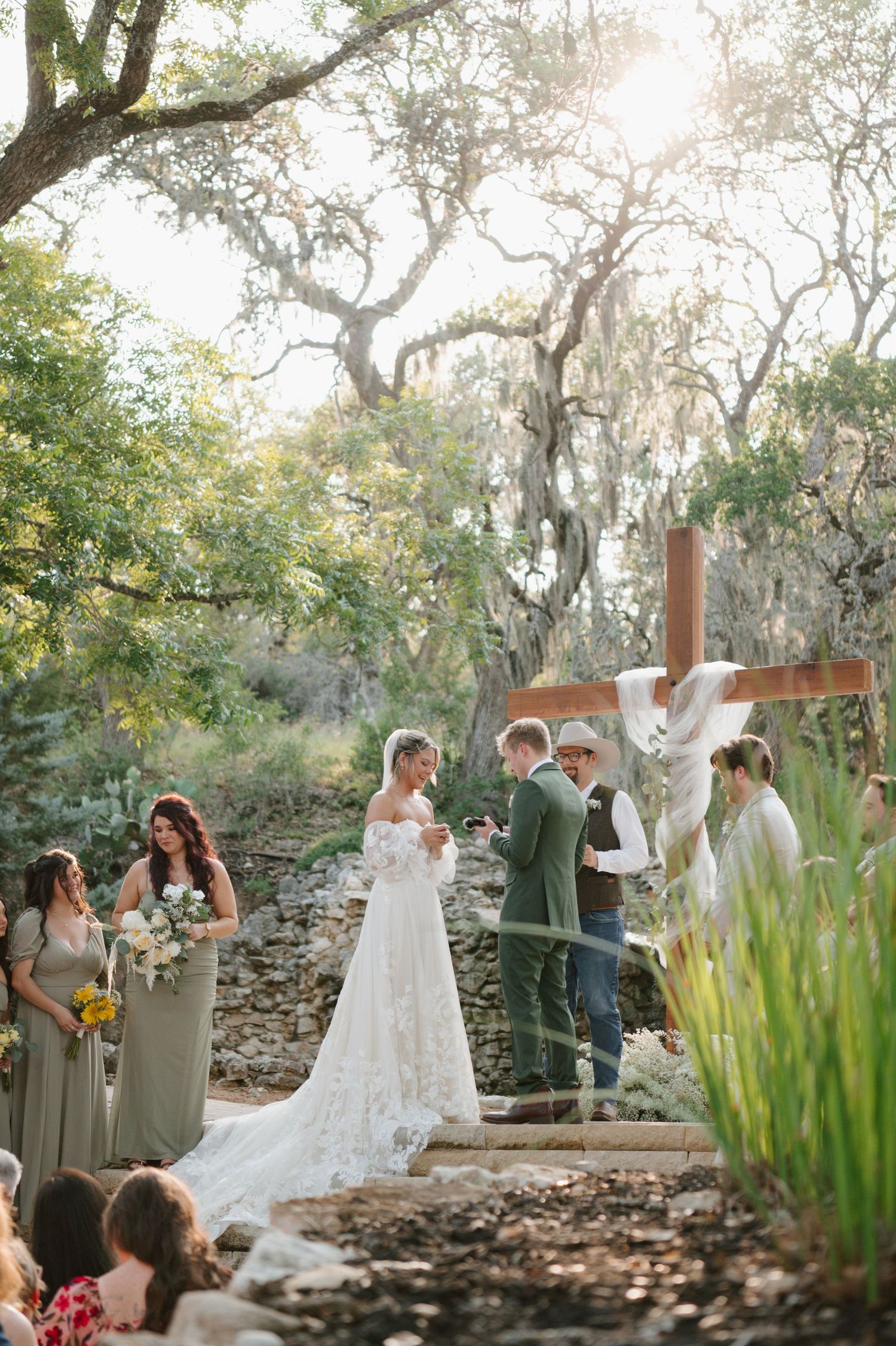 Outdoor wedding ceremony in a rustic garden setting with Spanish moss draped trees and stone pathway.