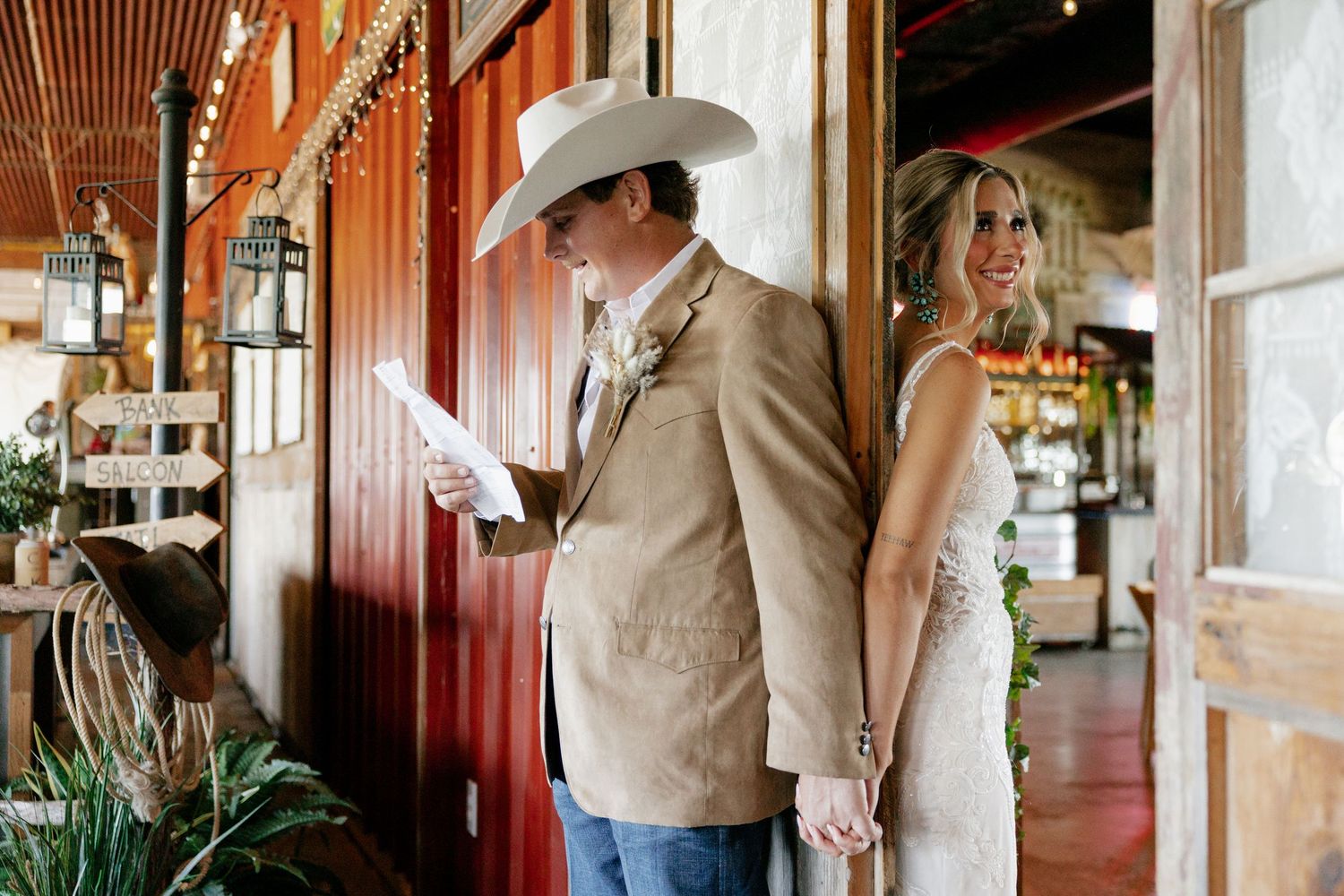 Western-themed wedding couple standing on rustic porch with cowboy hat and casual attire.