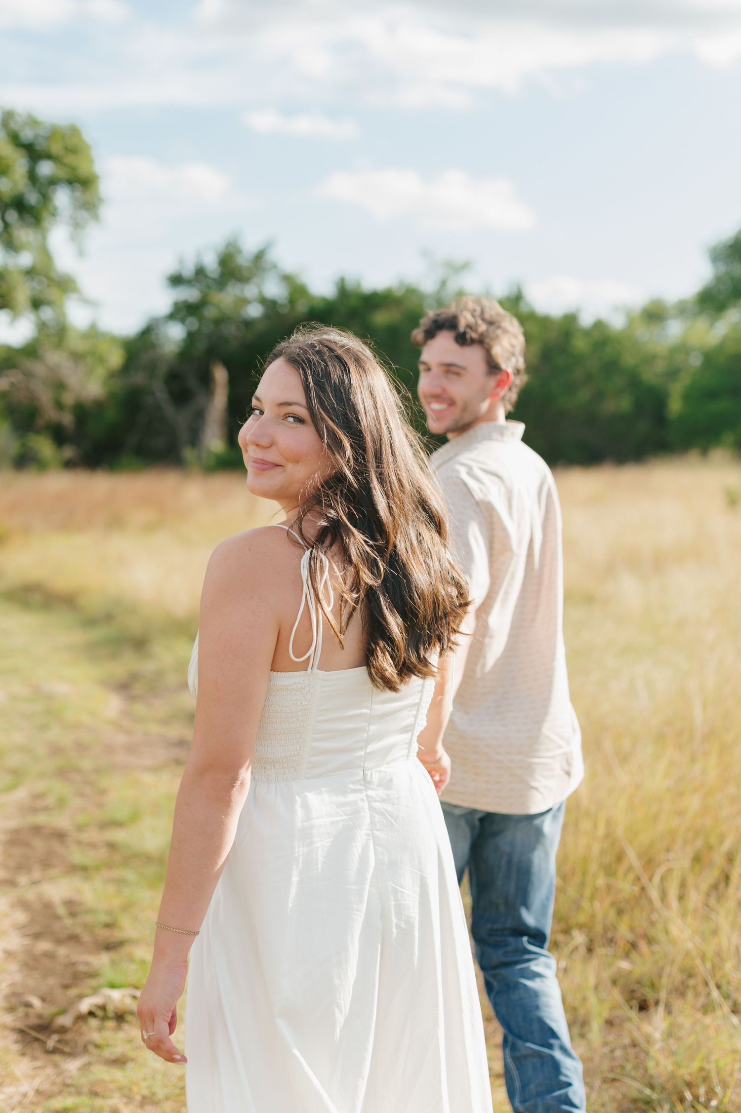Couple in white and beige outfits walking through a golden summer meadow.