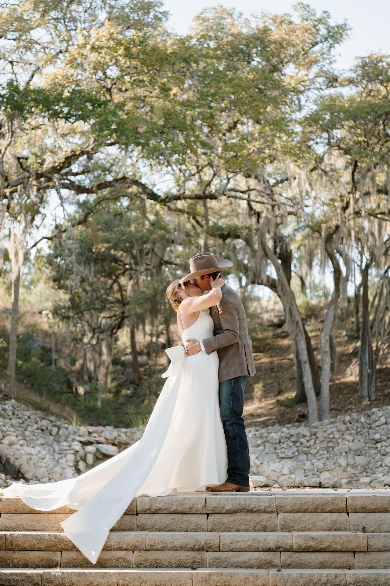Couple shares romantic moments on stone steps surrounded by trees in an outdoor setting.