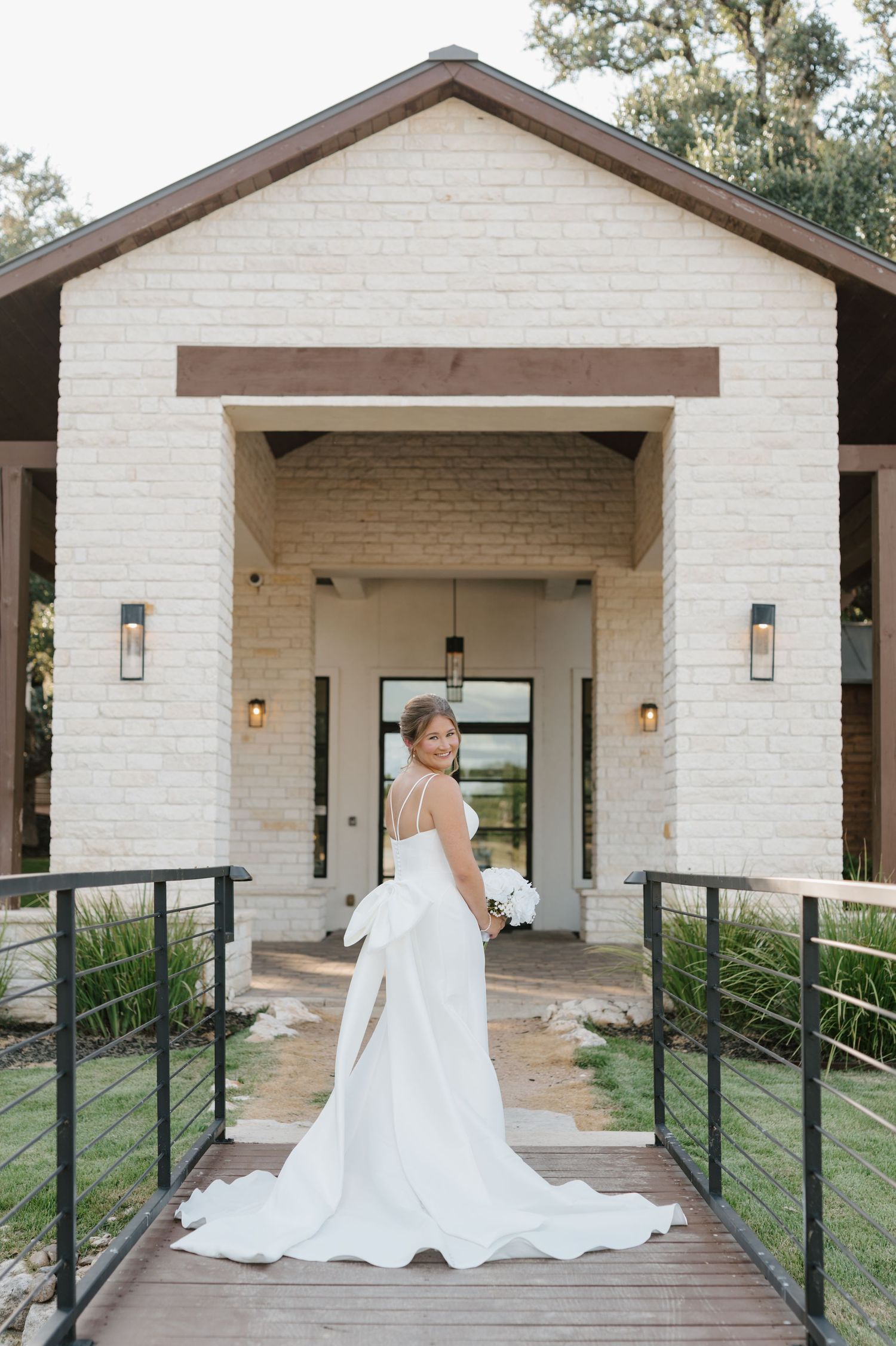 A stunning white bridal gown with a flowing train photographed on a modern covered porch with white brick walls.