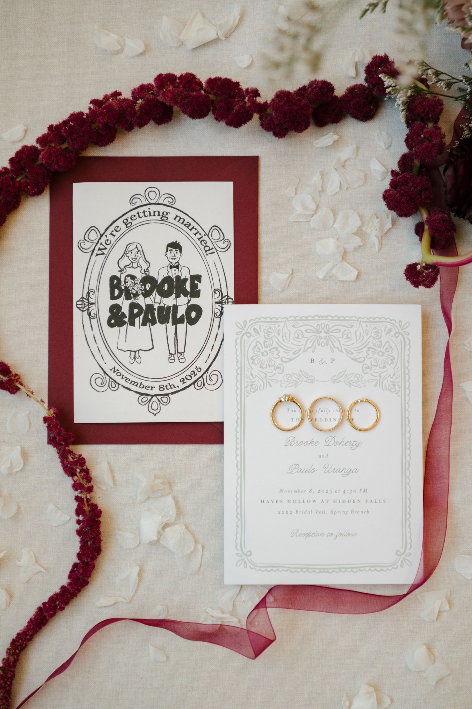Wedding invitation suite with burgundy flowers and gold rings on white textured paper.