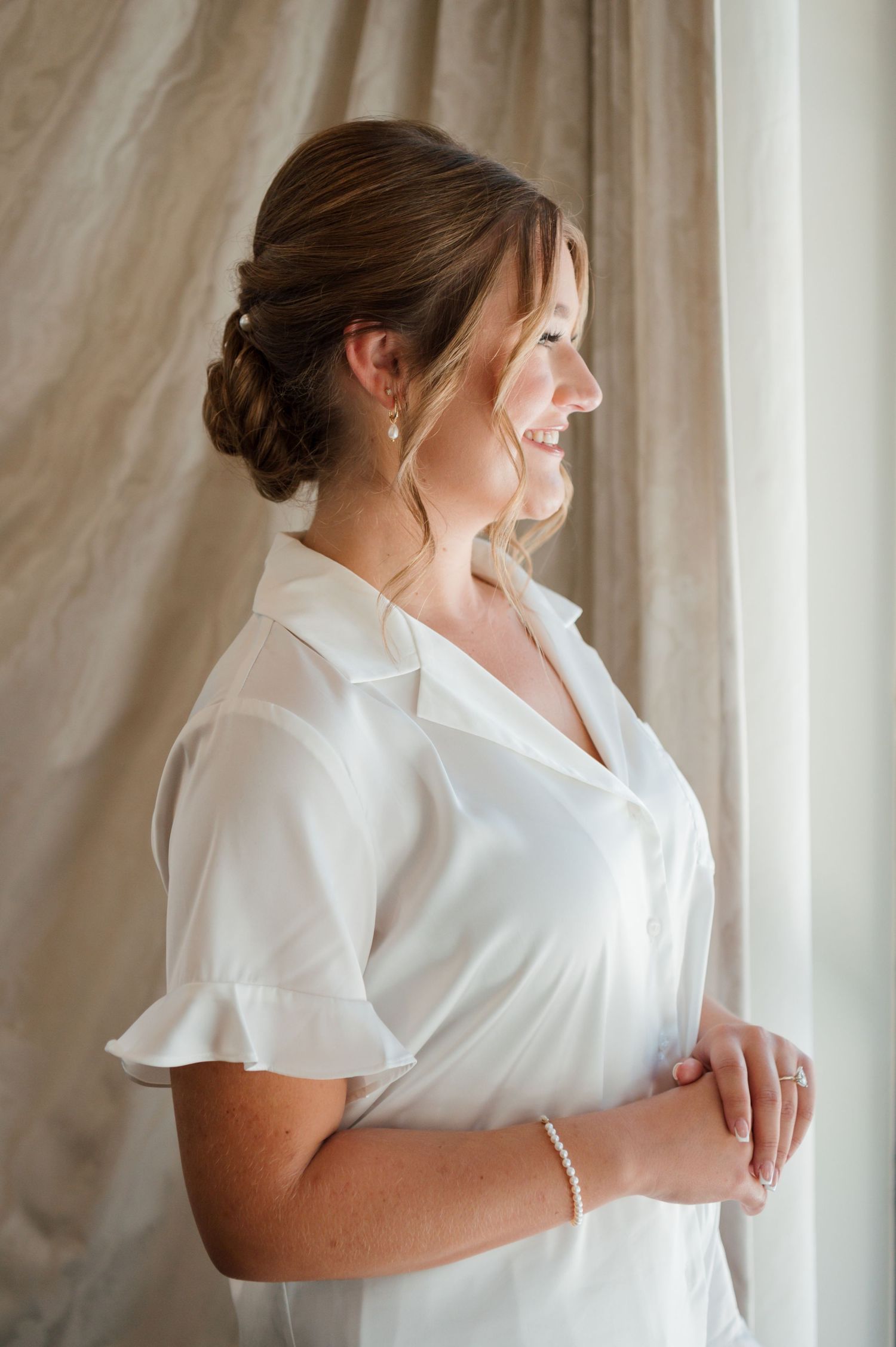Bride in a white dress poses by a window in a series of elegant getting ready shots.