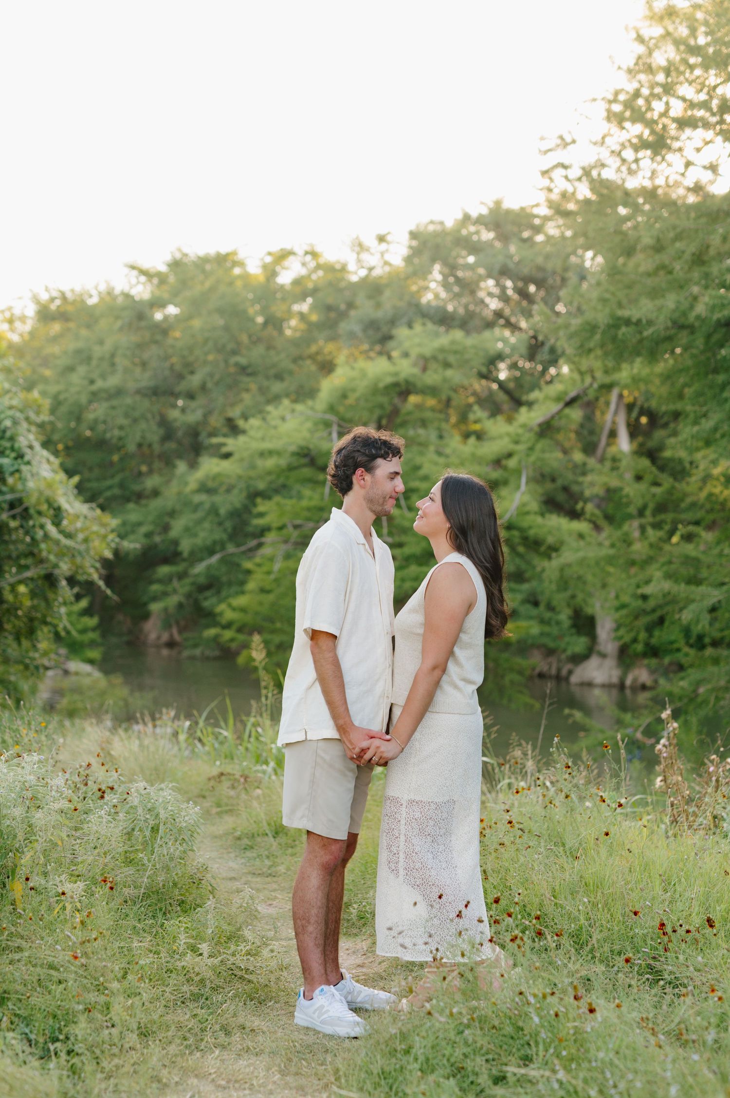 A couple in white outfits sharing tender moments in a wildflower meadow at sunset.