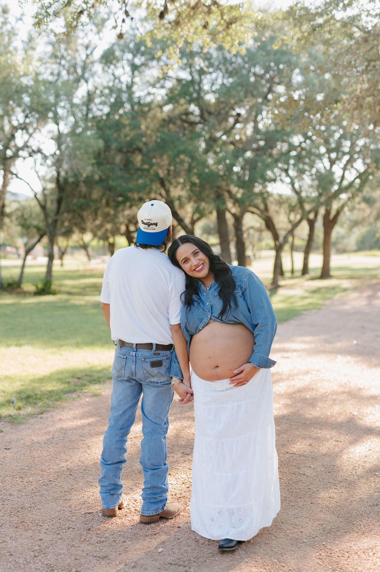 Candid maternity photography session shows playful moments on a dirt path surrounded by trees.