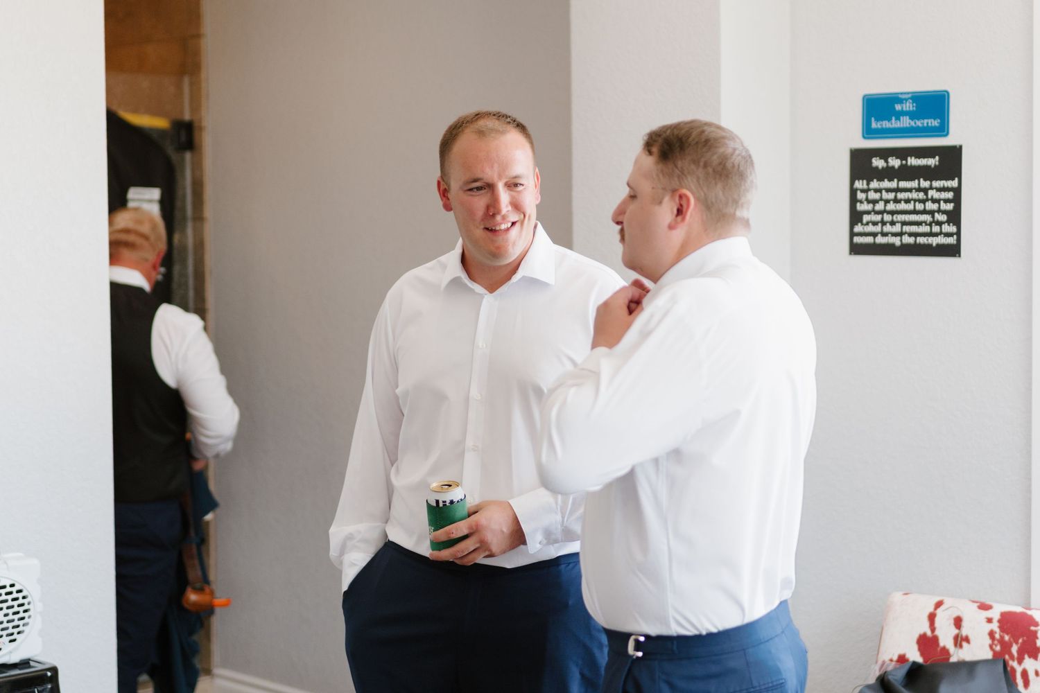 Two people in white dress shirts socialize at a casual indoor event while holding drinks.