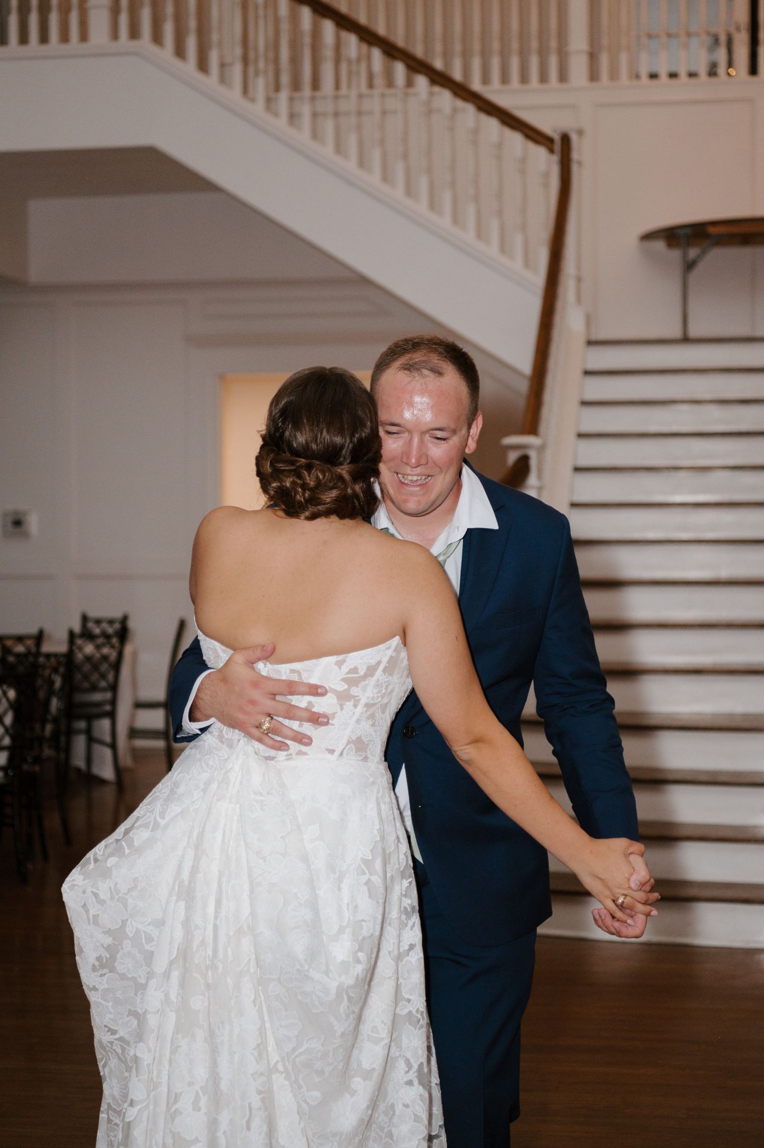 Couple sharing an intimate dance moment near an elegant white staircase.
