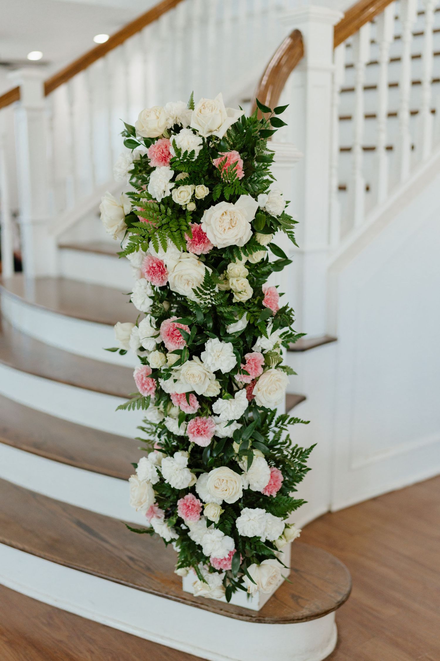 Elegant floral arrangements with pink and white roses decorate a white staircase in a wedding venue.