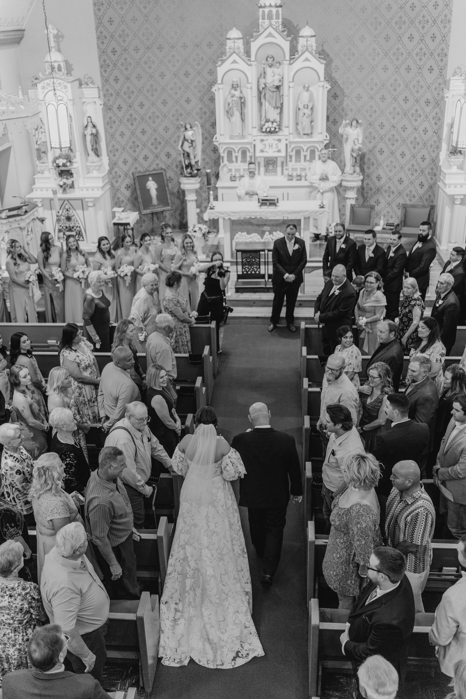 Black and white vintage church wedding ceremony with guests seated in pews and ornate altar in background.