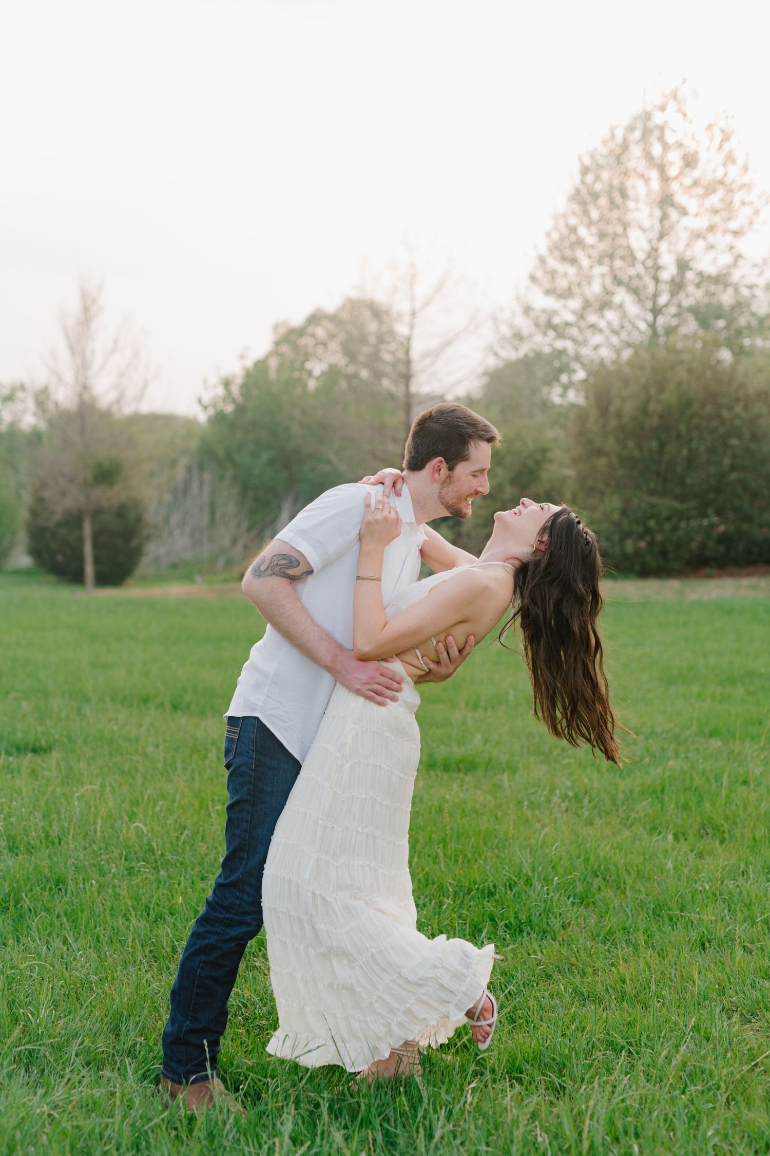 A romantic couple dances in a grassy meadow on a spring evening, with trees in the background.