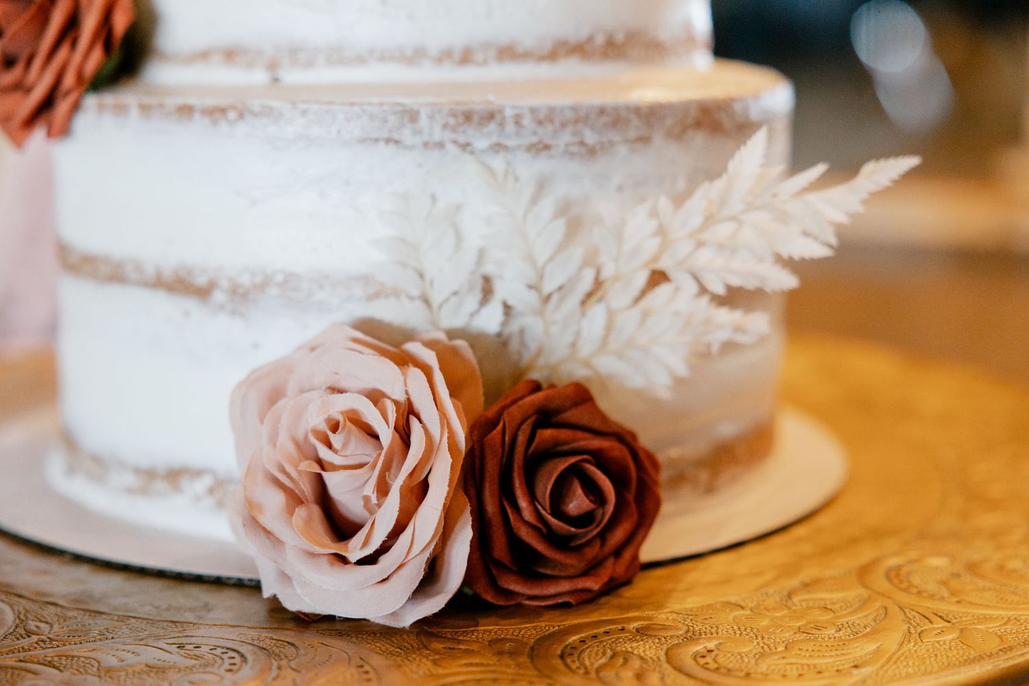 White wedding cake decorated with pink and brown roses and delicate fern leaves.