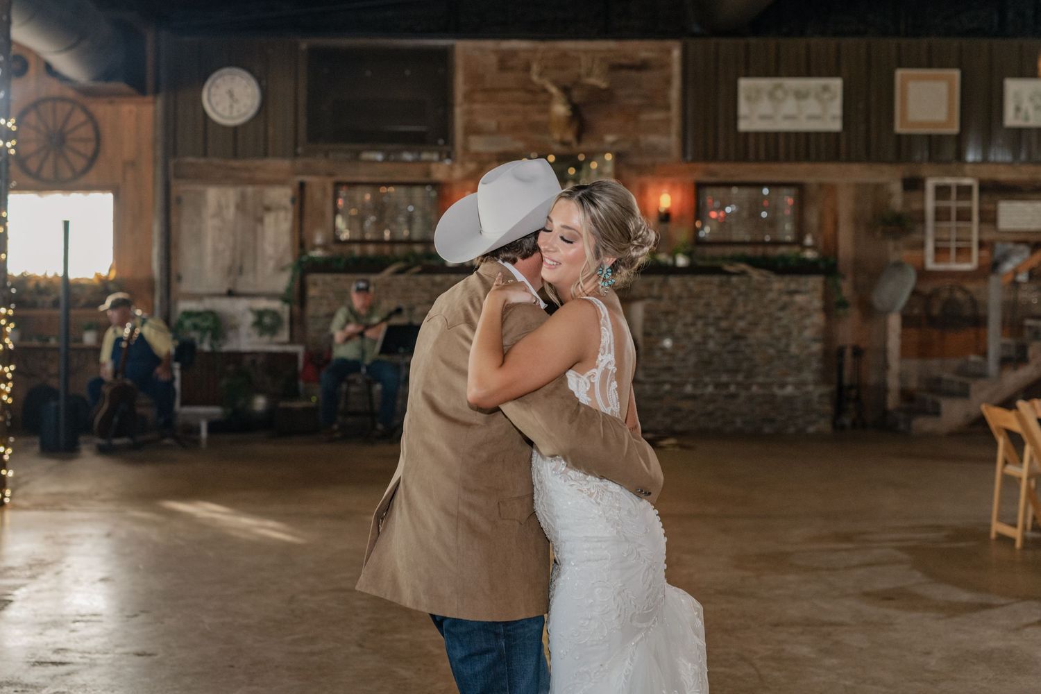 A tender embrace between newly weds sharing a kiss during their first dance in a rustic barn venue with stone walls.