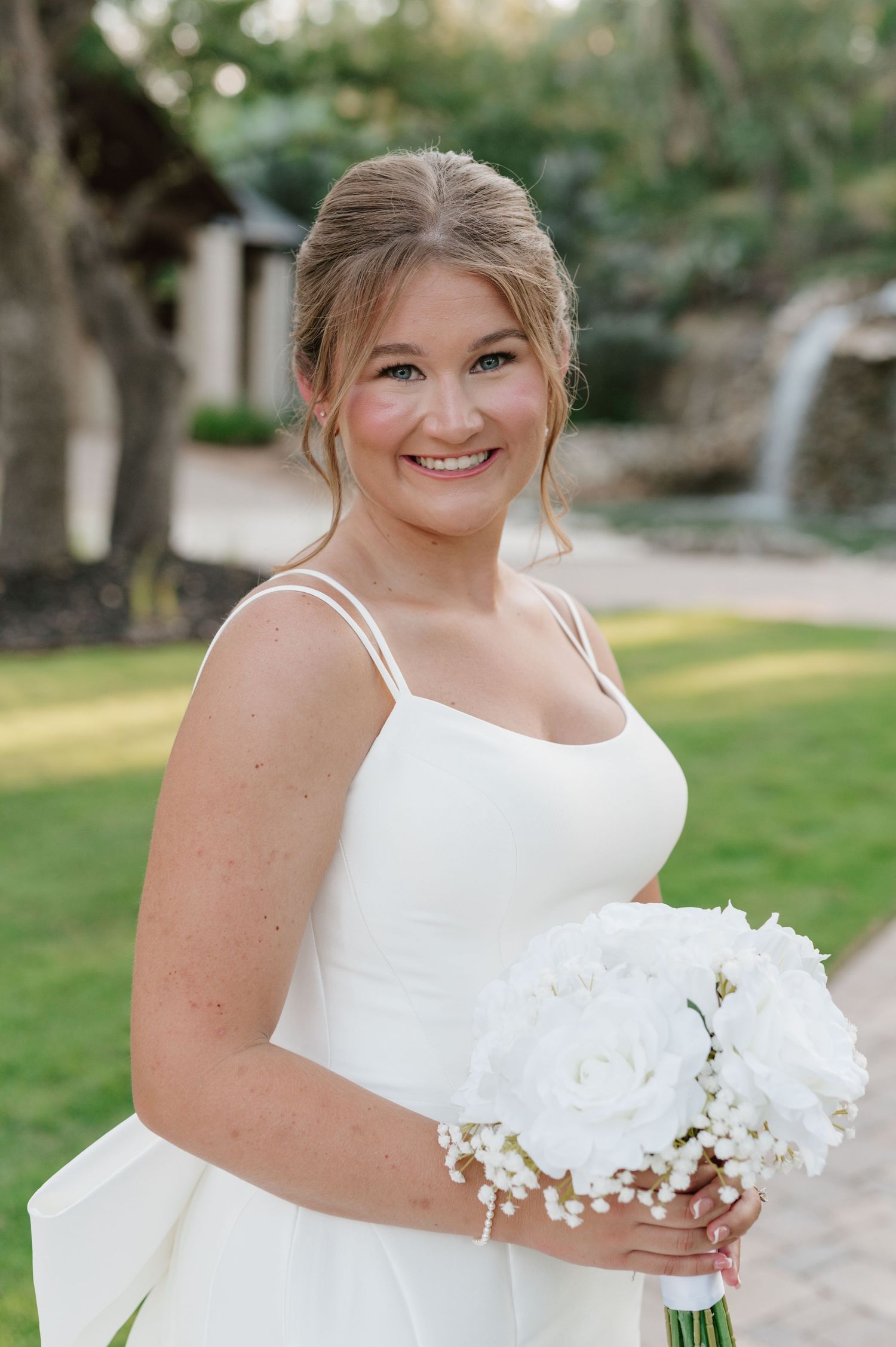 Bride in a modern white wedding gown poses with bouquet in a garden setting.