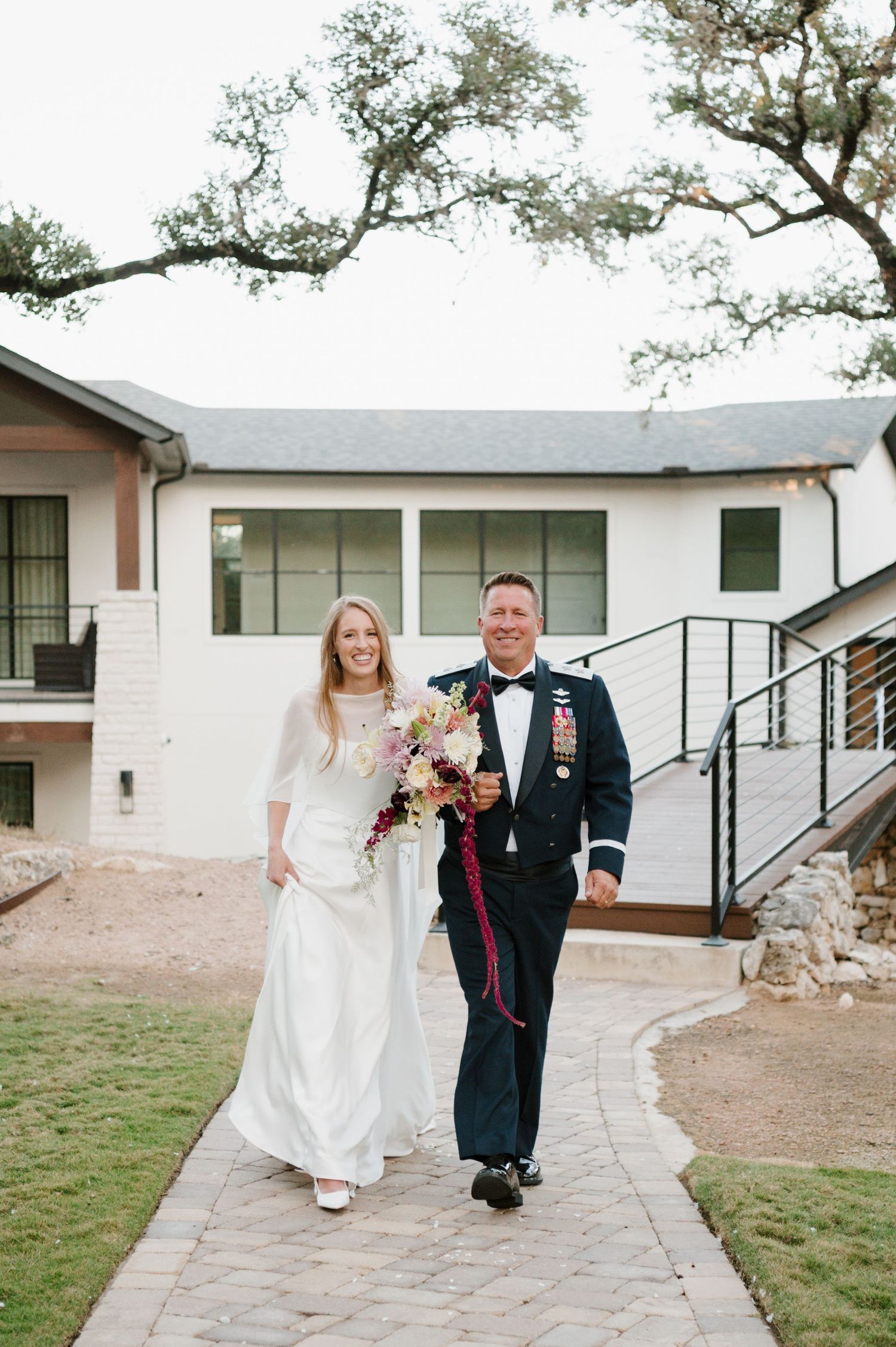 Couple walks along white concrete pathway outside modern building on their wedding day.