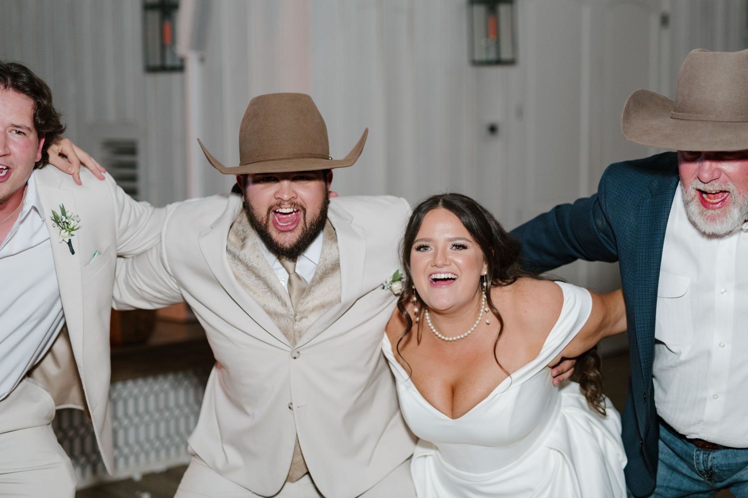 A joyful group in western attire and formal wear celebrate together at an indoor wedding reception.