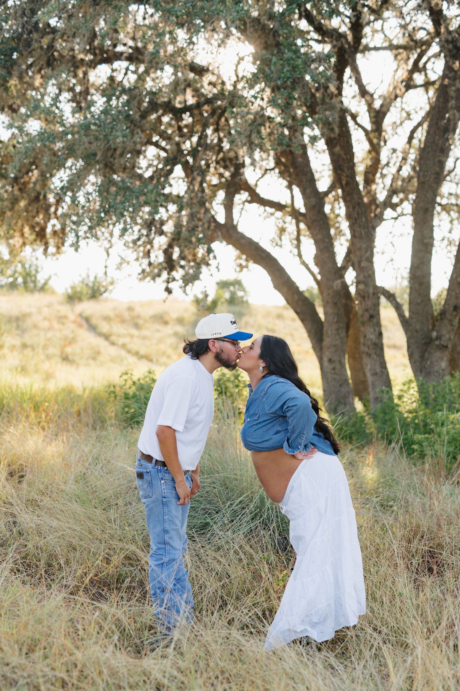 A romantic outdoor photoshoot among tall grass and oak trees during golden hour.