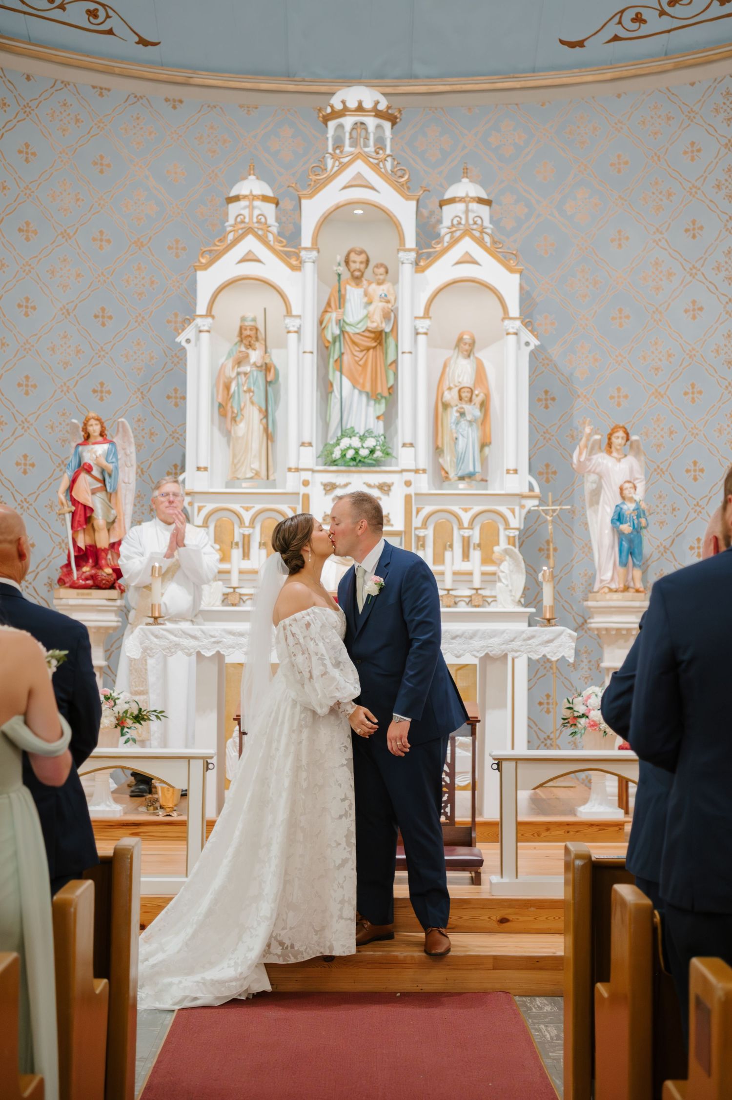 Catholic church altar with ornate religious statues and blue walls during wedding ceremony.