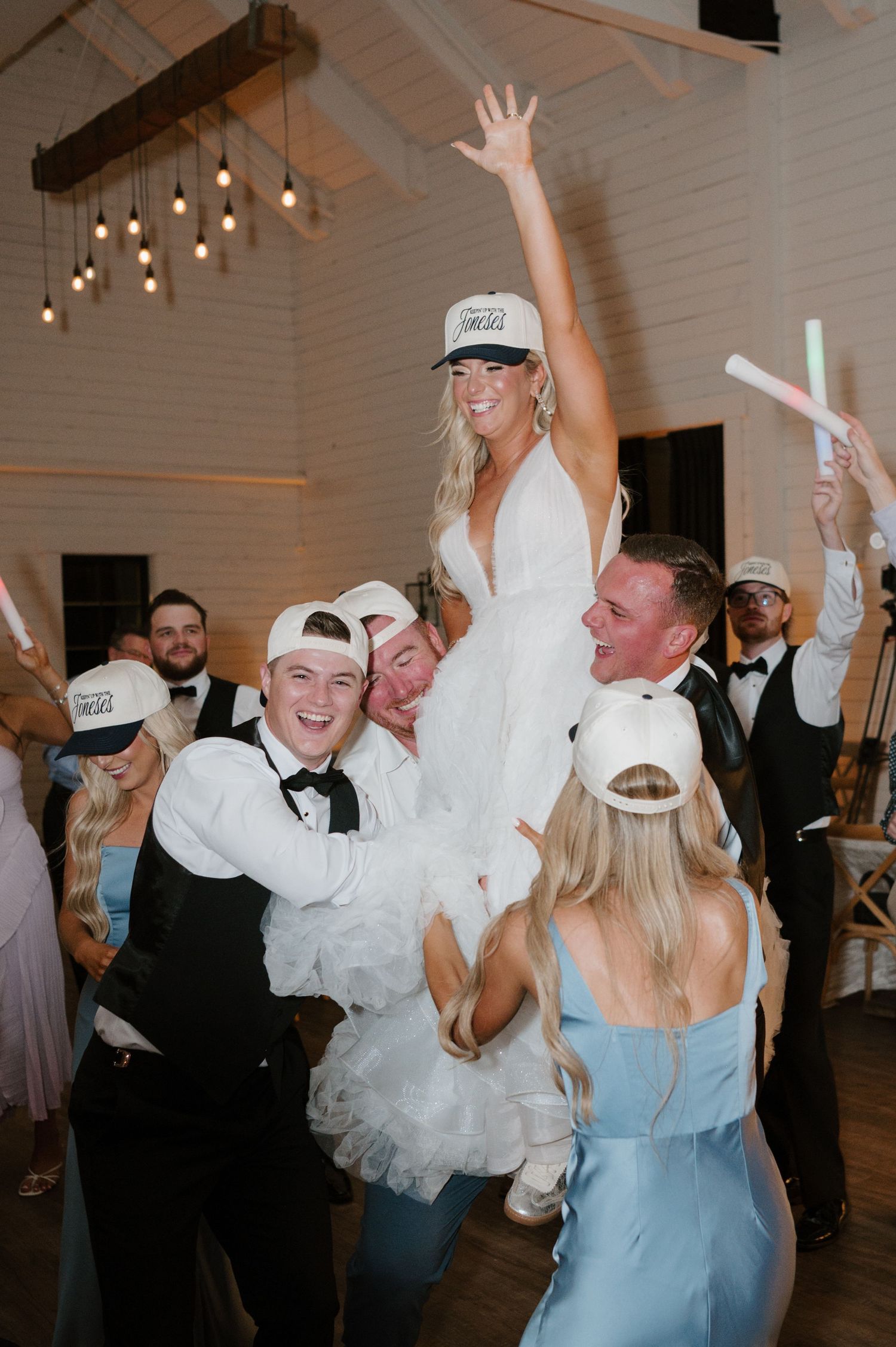 A bride wearing a white wedding dress is lifted up by wedding guests at a celebration.