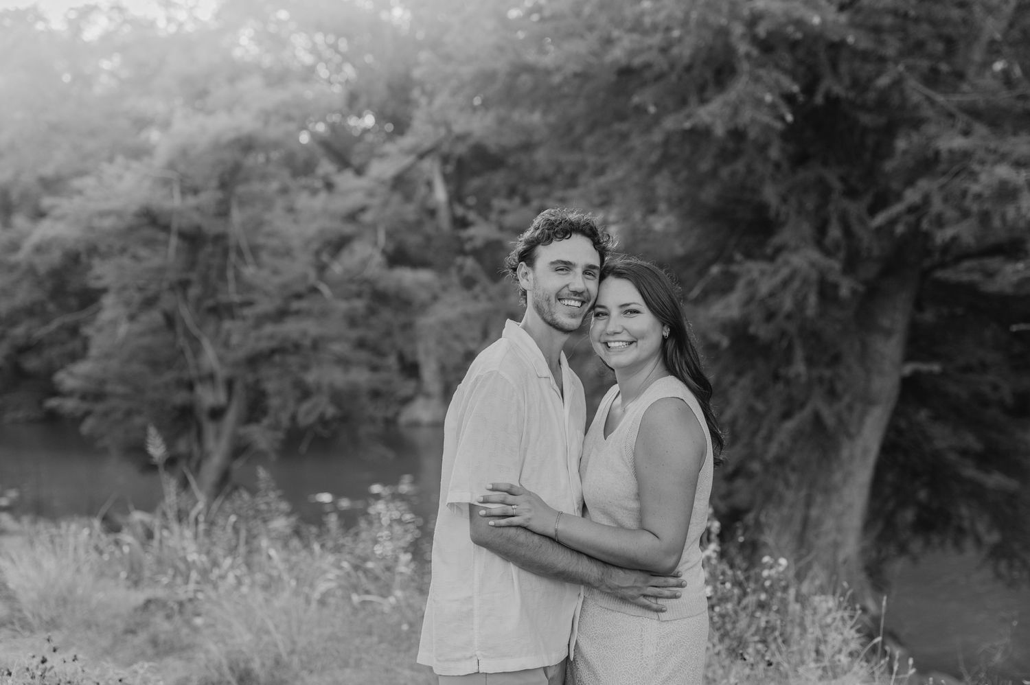 A romantic black and white portrait of a couple embracing in a natural outdoor setting.