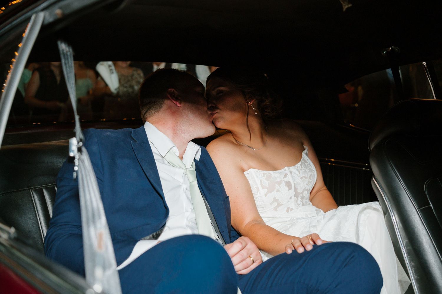 Couple departing wedding reception in car decorated with string lights at night.