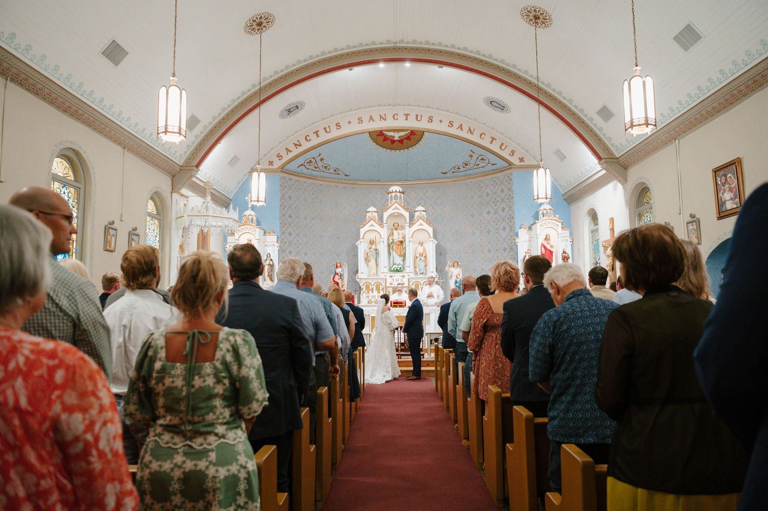 Traditional church interior with wooden pews and vaulted ceiling filled with wedding guests.