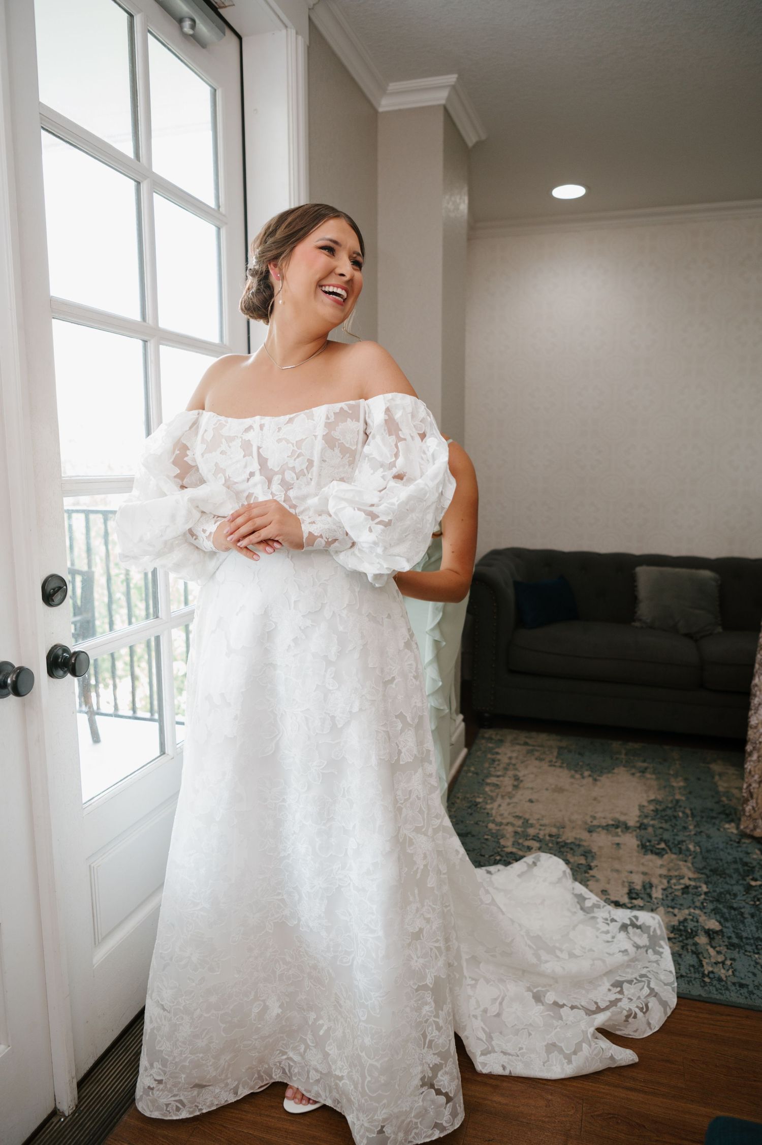 Wedding dress with delicate lace details laid out across a hardwood floor near bright windows.