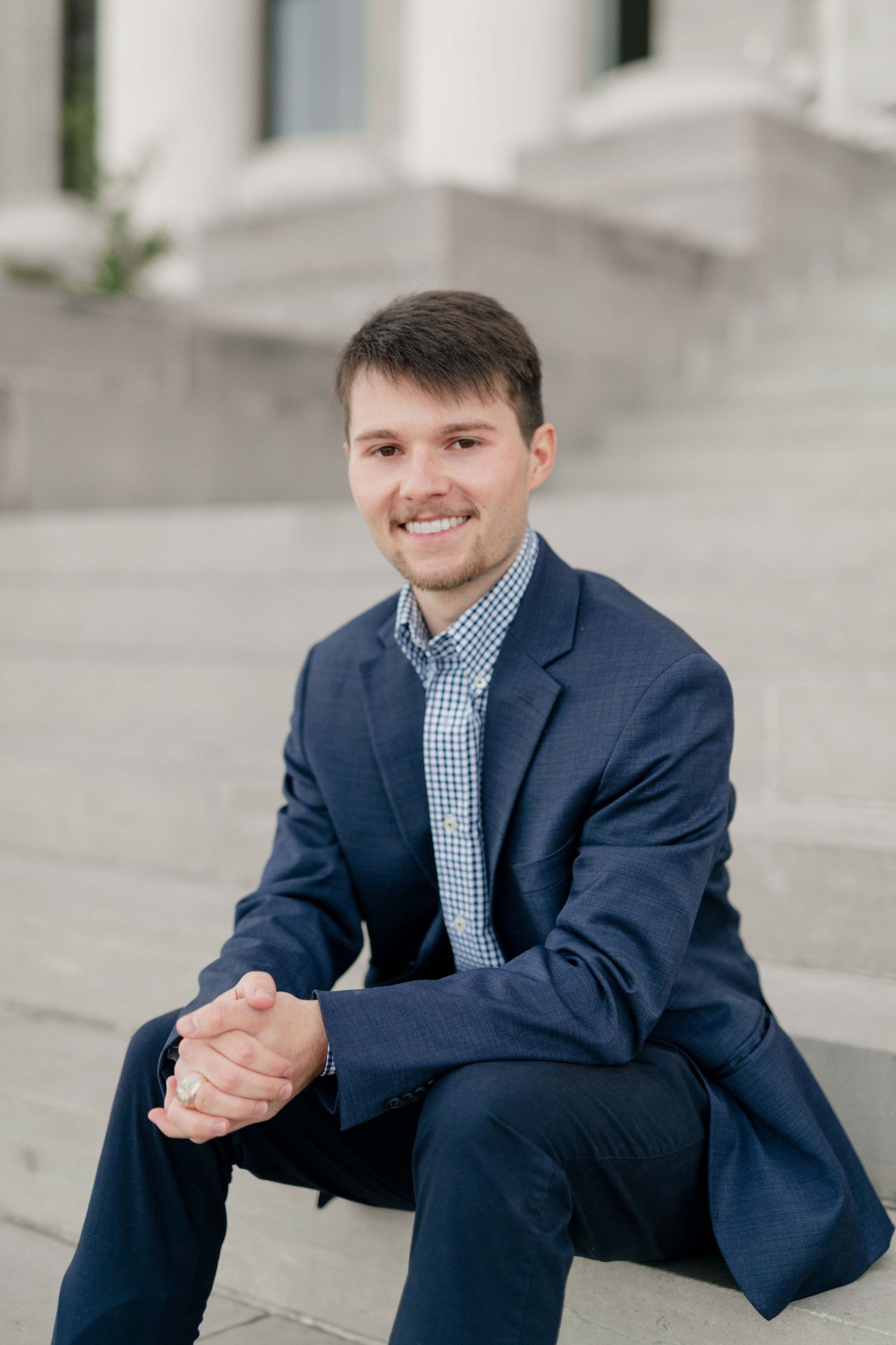 Professional portrait of person in navy suit sitting on white stone steps.
