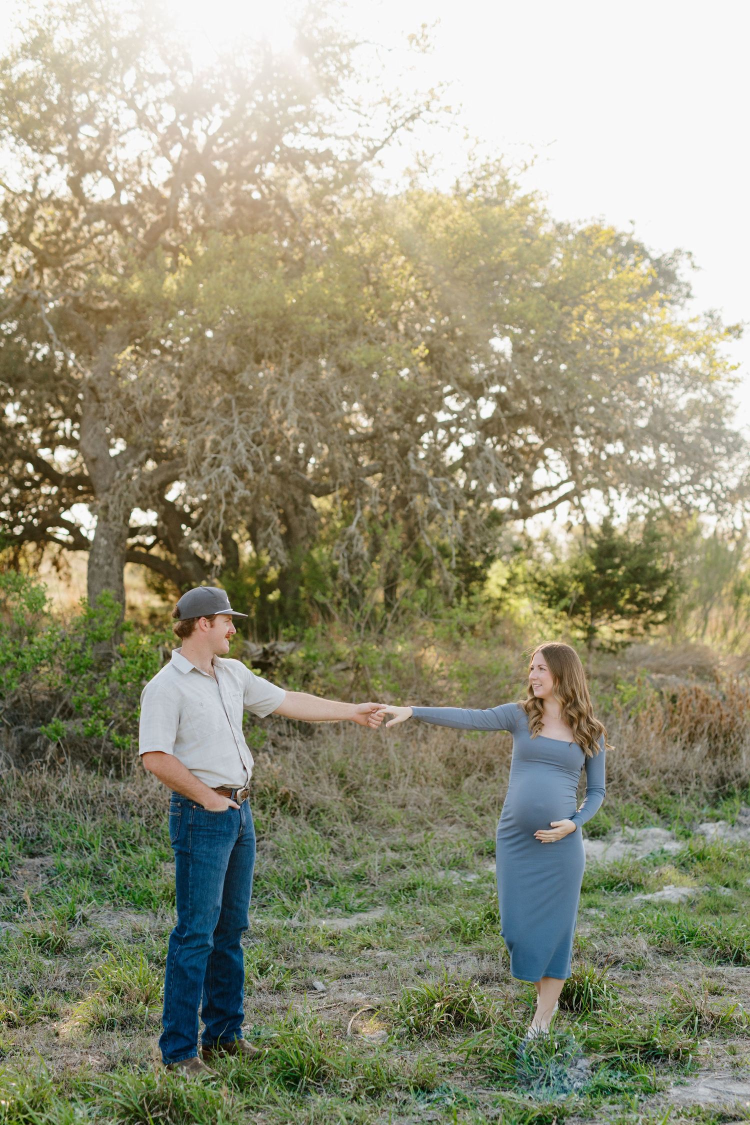 A couple poses together outdoors in a natural setting during golden hour, with the woman wearing a blue dress.