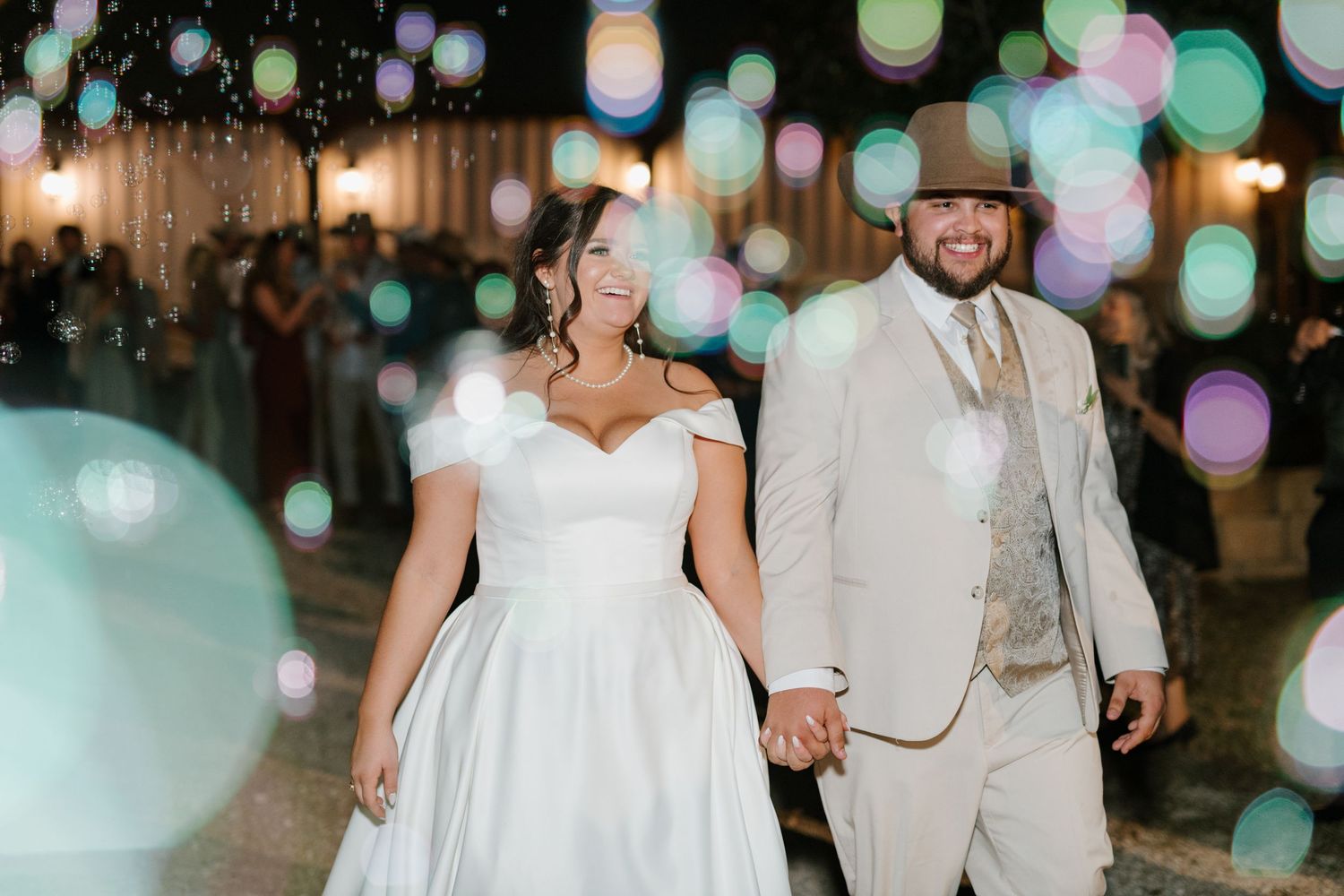 A couple enjoys their wedding reception under glowing lanterns and colorful bokeh lights at night.