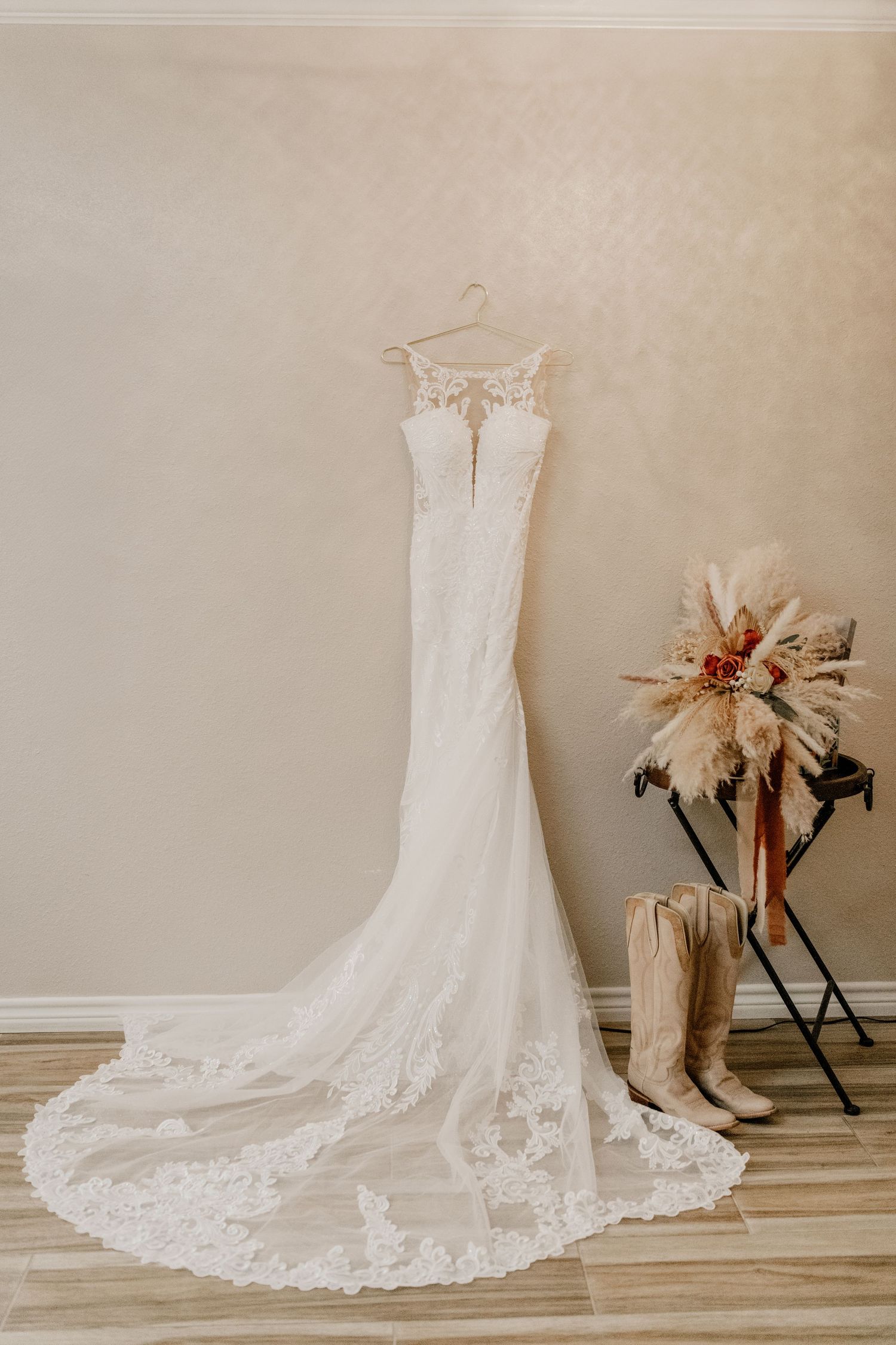 Elegant white lace wedding dress with sweetheart neckline and long train hanging beside dried floral arrangement.