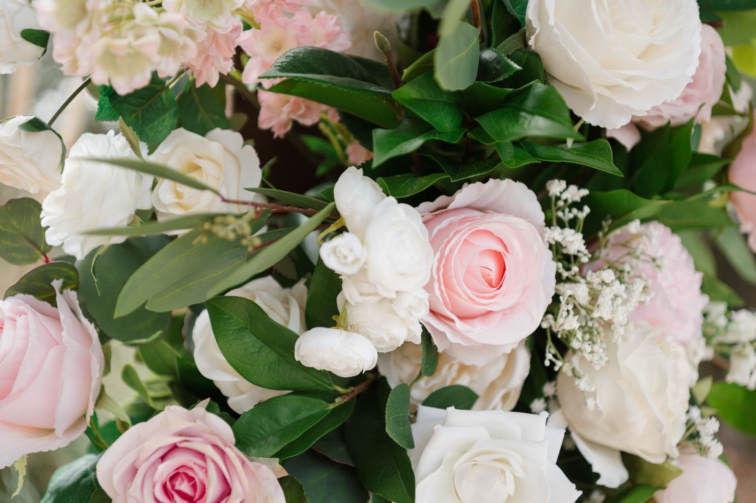 A lush floral arrangement featuring pink and white roses with delicate green foliage and eucalyptus leaves.