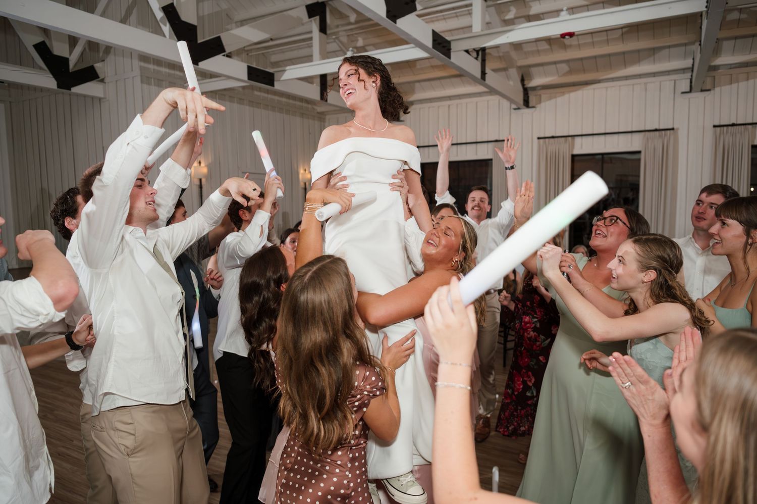 Wedding reception celebration with guests dancing and cheering under industrial ceiling.