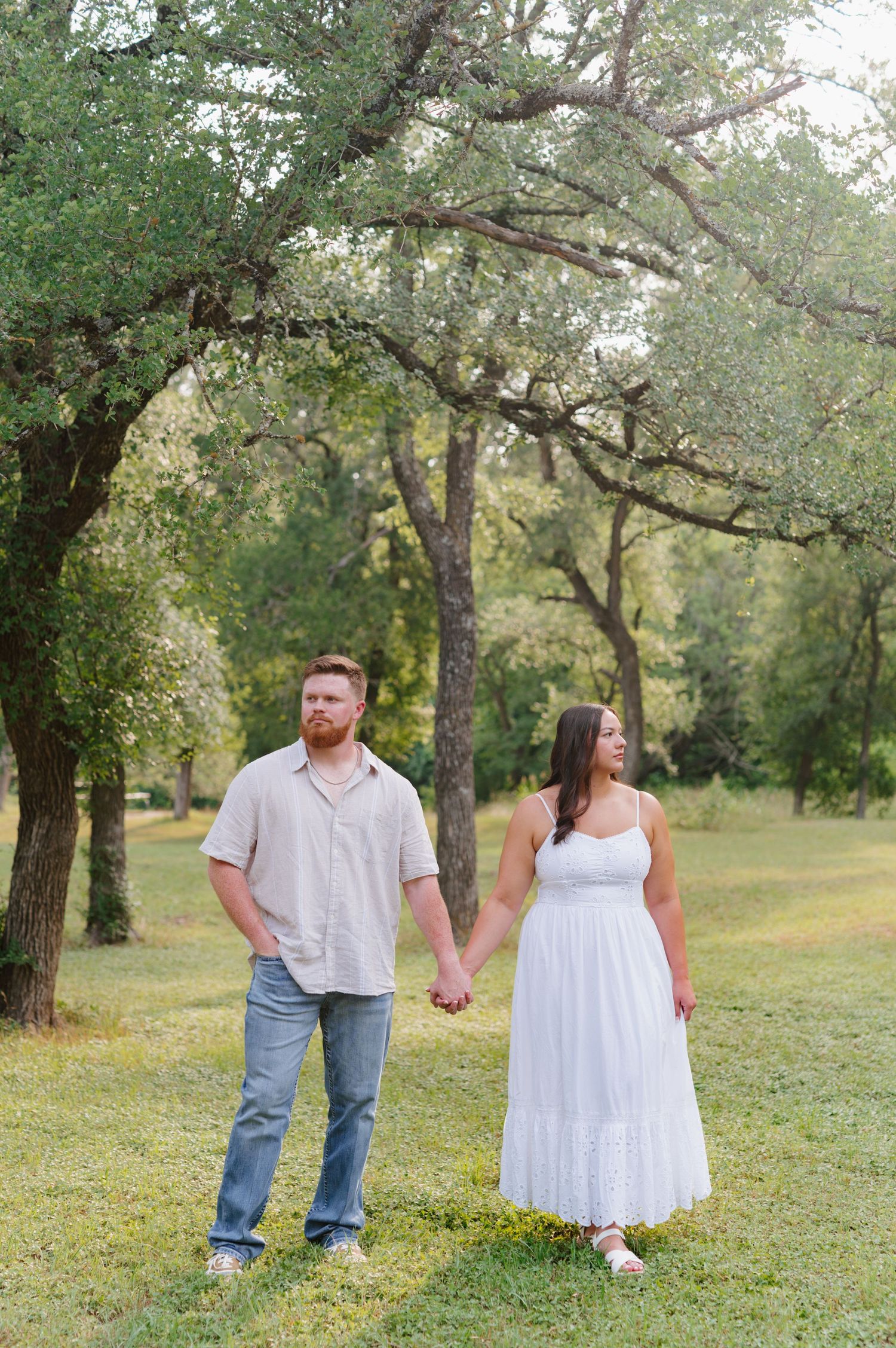 Couple walks and poses together in a scenic outdoor park setting with lush green trees.
