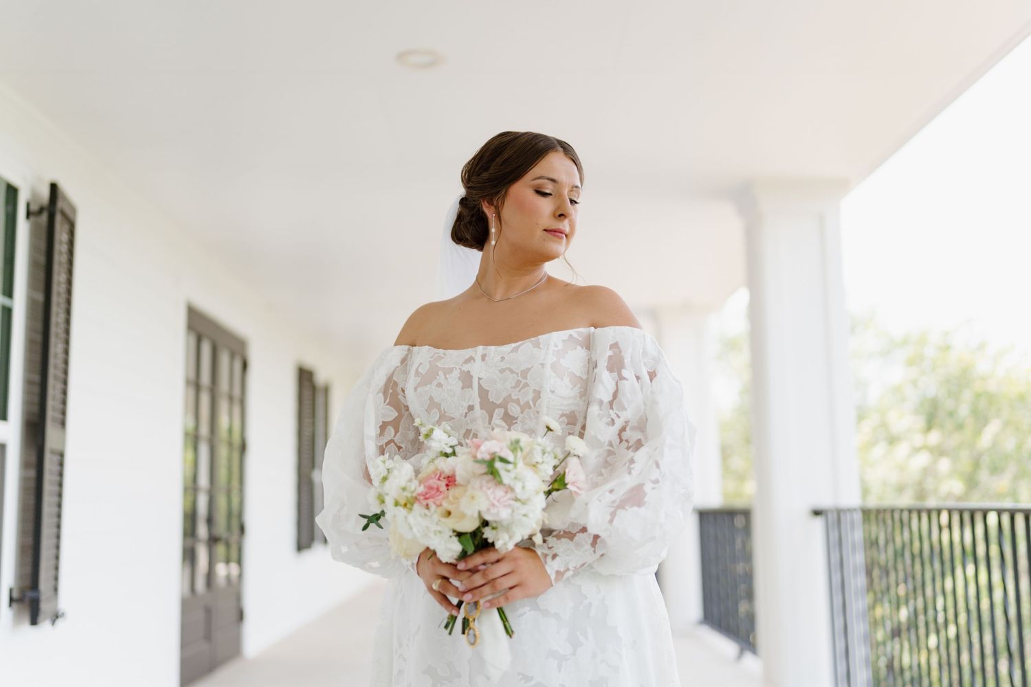 An elegant white bridal gown displayed on a bright Southern-style covered porch with black shutters.
