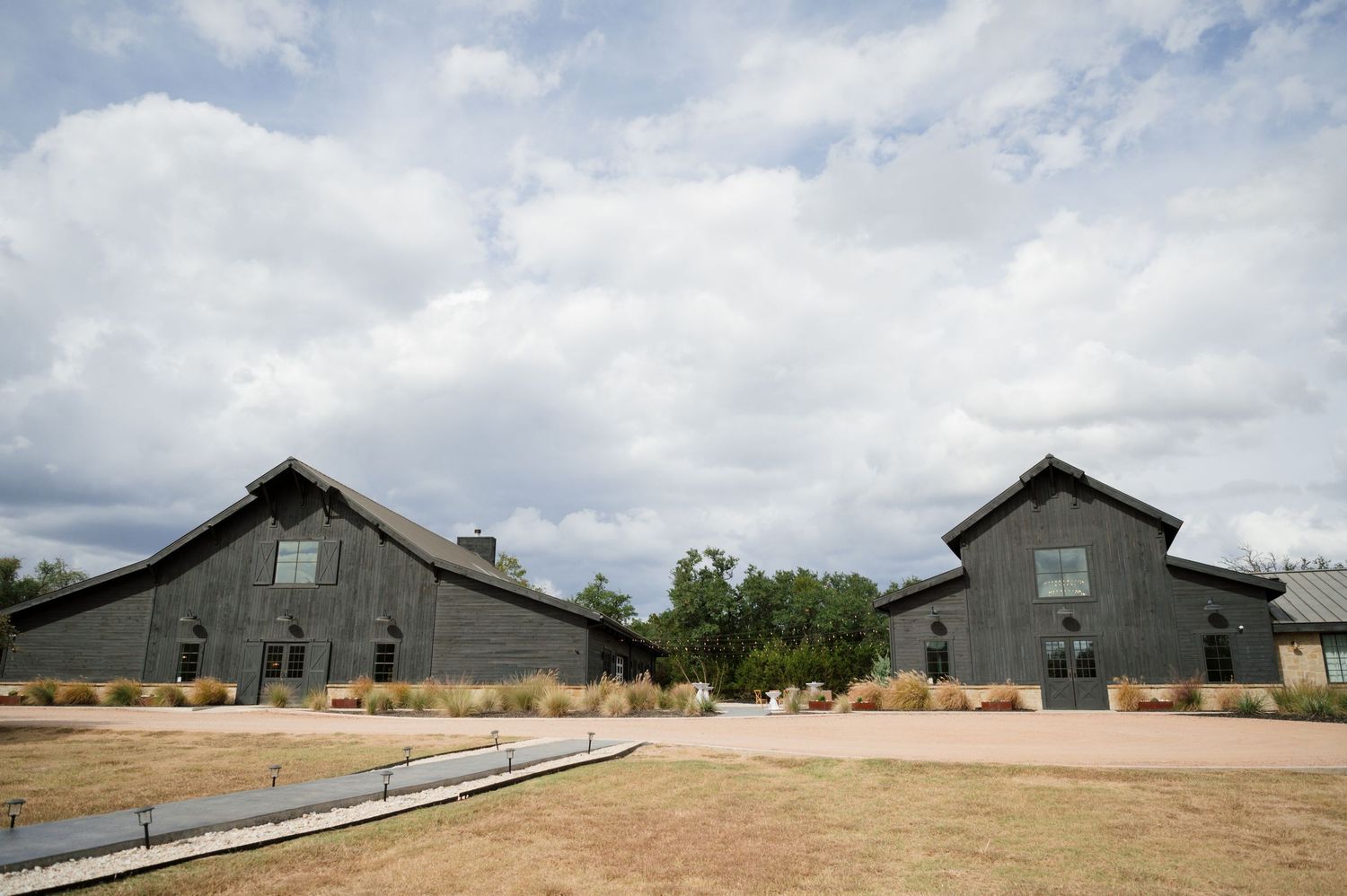 Two large barns with wooden siding and tin roofs in a rural setting.