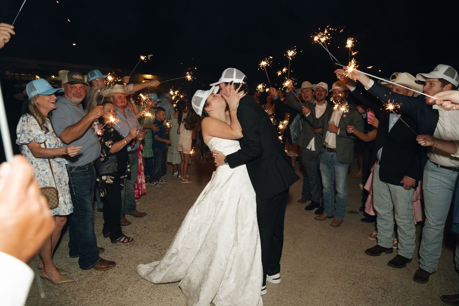 Newlywed couple shares a kiss during a sparkler send-off at their outdoor night wedding celebration.