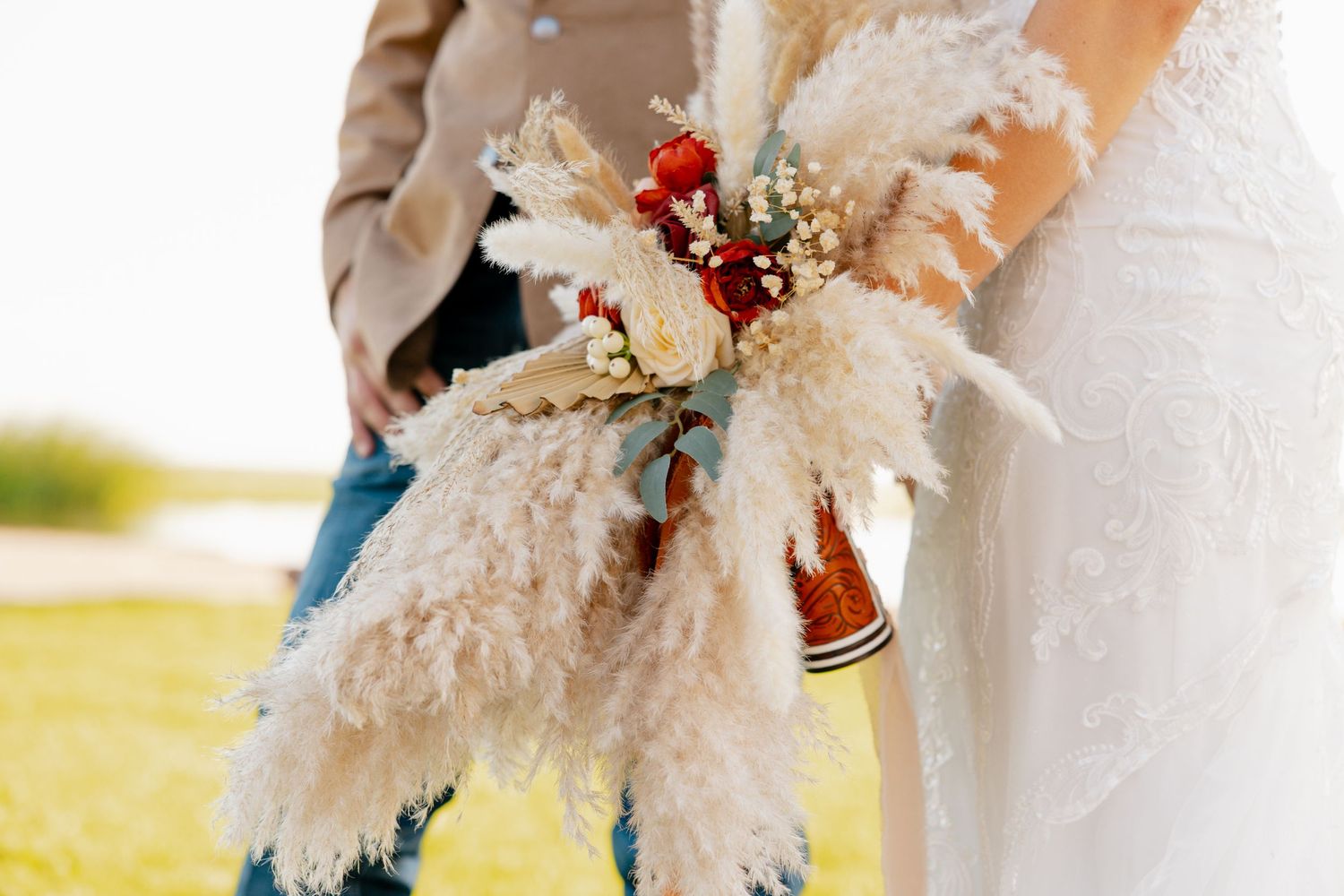 A rustic wedding bouquet featuring fluffy pampas grass, dried flowers, and red berries in a bohemian style arrangement.
