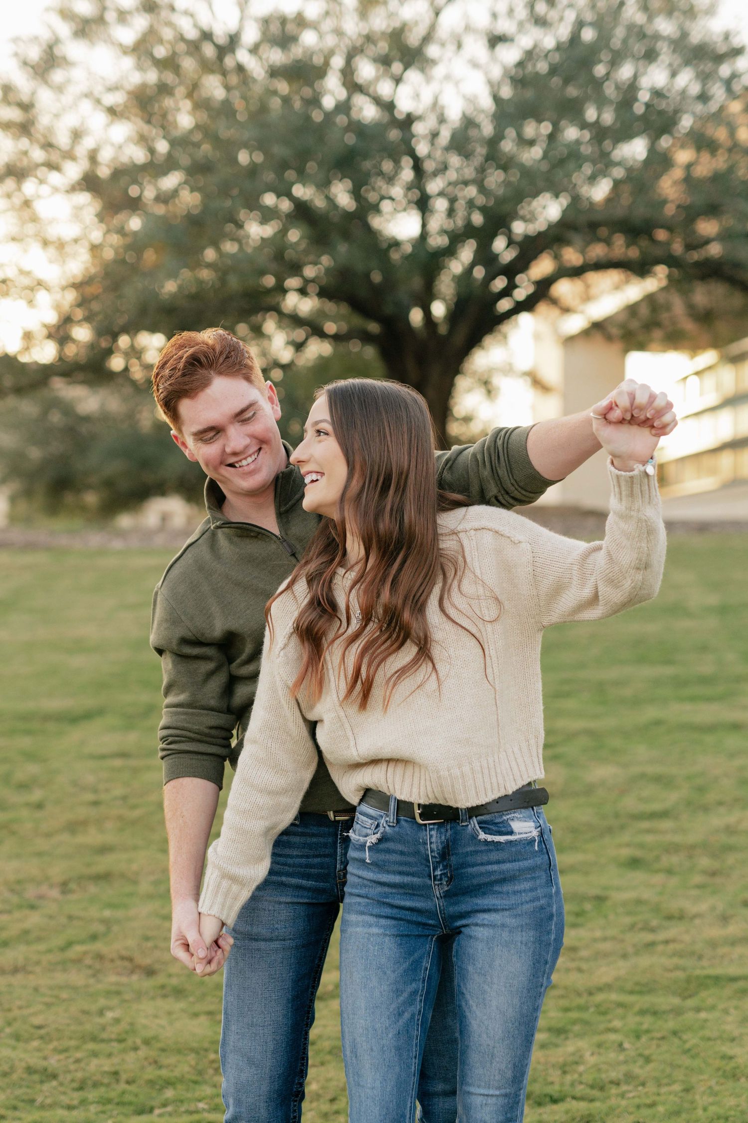 A couple dances and laughs together on a grassy hill during golden hour.