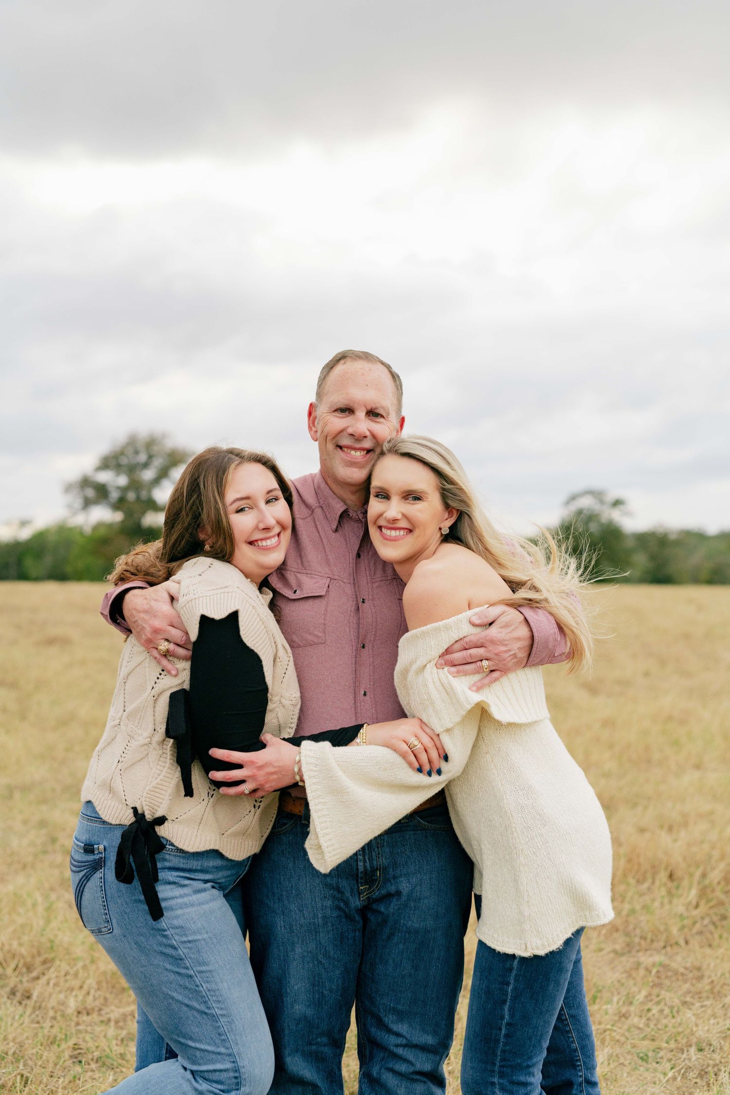 Candid portrait of three people embracing and laughing in a field.