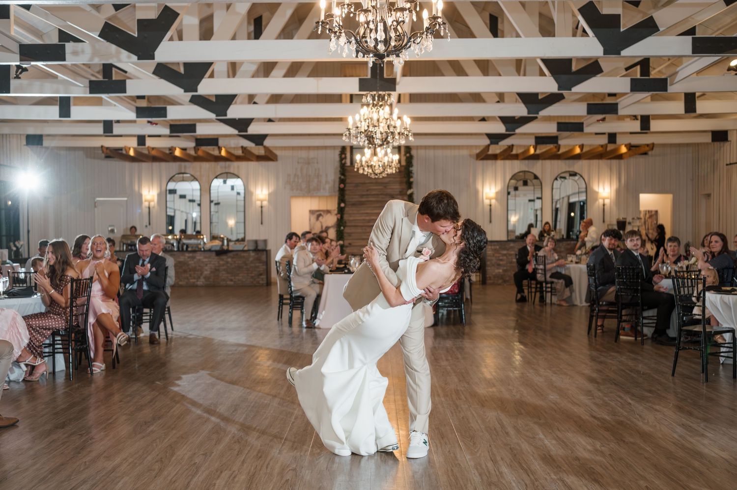 Wedding reception venue with exposed beams, chandeliers, and wooden dance floor.