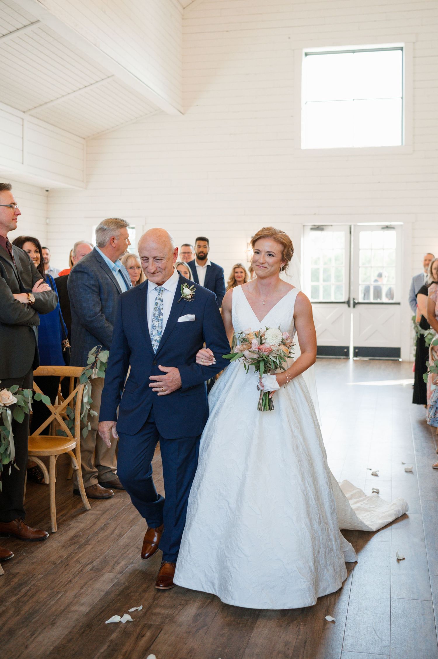 A couple shares their first dance in an elegant white wedding venue with high ceilings and wooden floors.